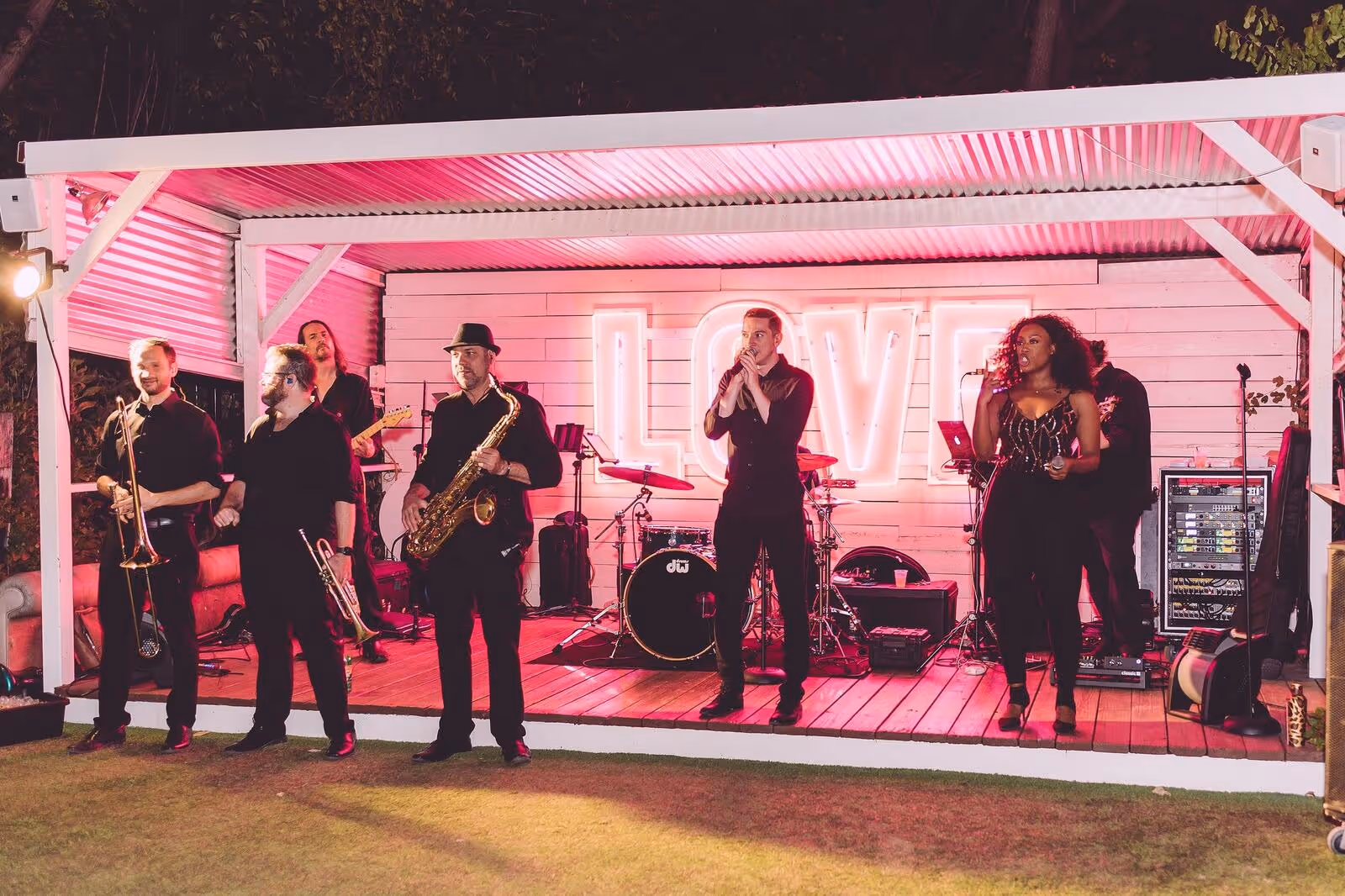 Live band performing on the open-air LOVE neon stage at Hotel Otto with pink stage lighting at night