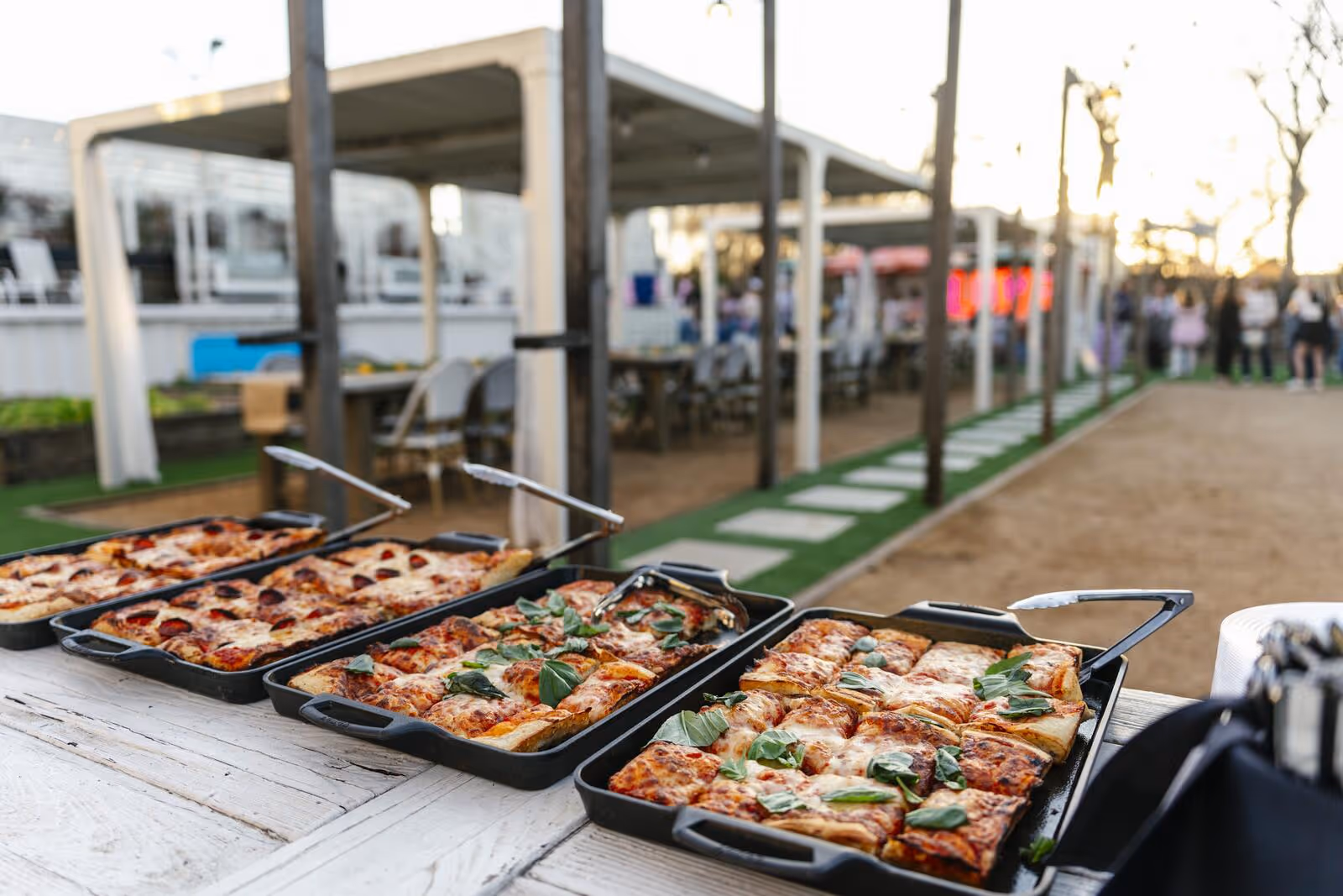 Detroit-style pizzas with basil garnish on a buffet table at sunset with the Hotel Otto LOVE sign glowing in the distance