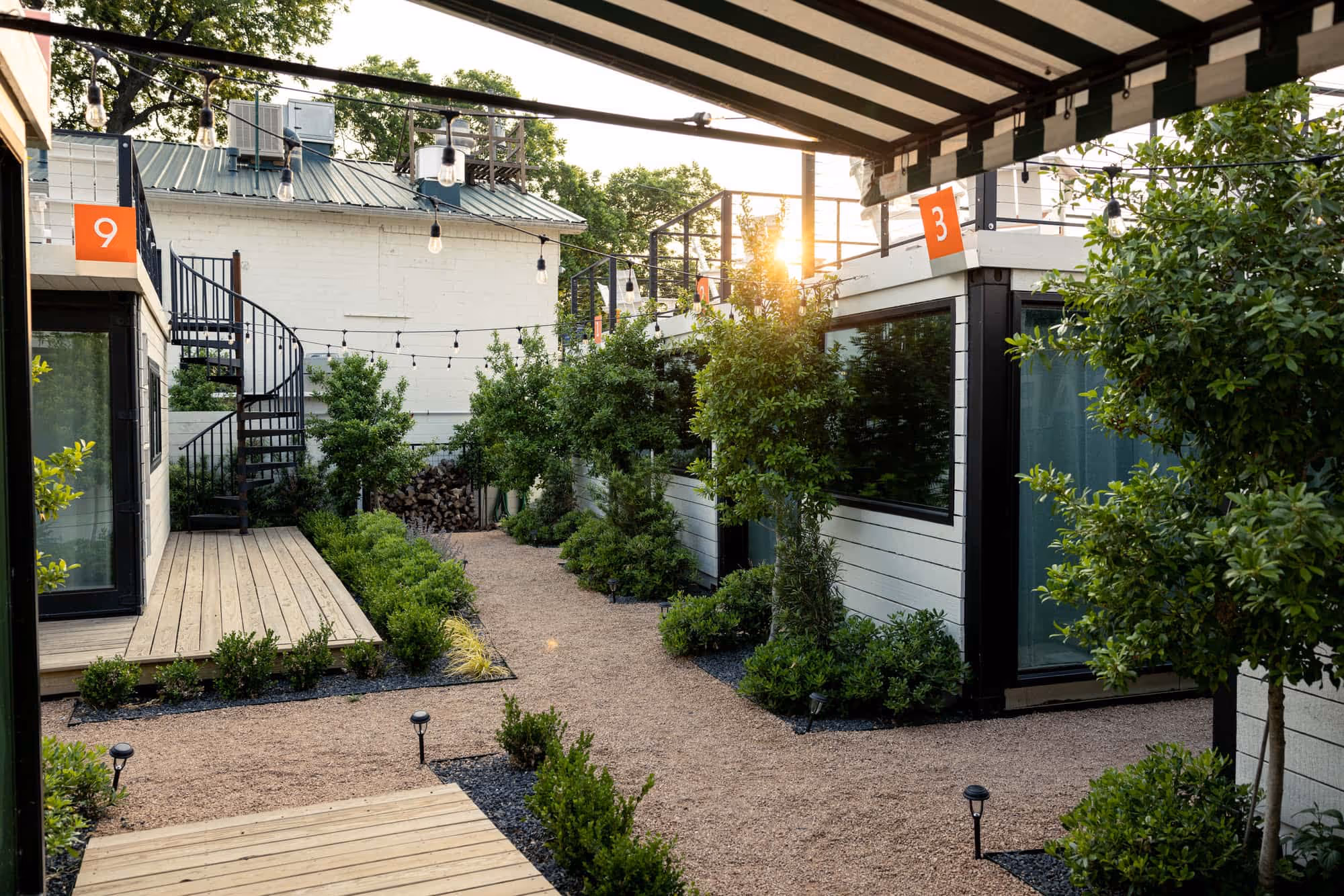 Hotel Otto courtyard at sunset, container bungalows numbered 9 and 3, gravel pathway, string lights, lush landscaping