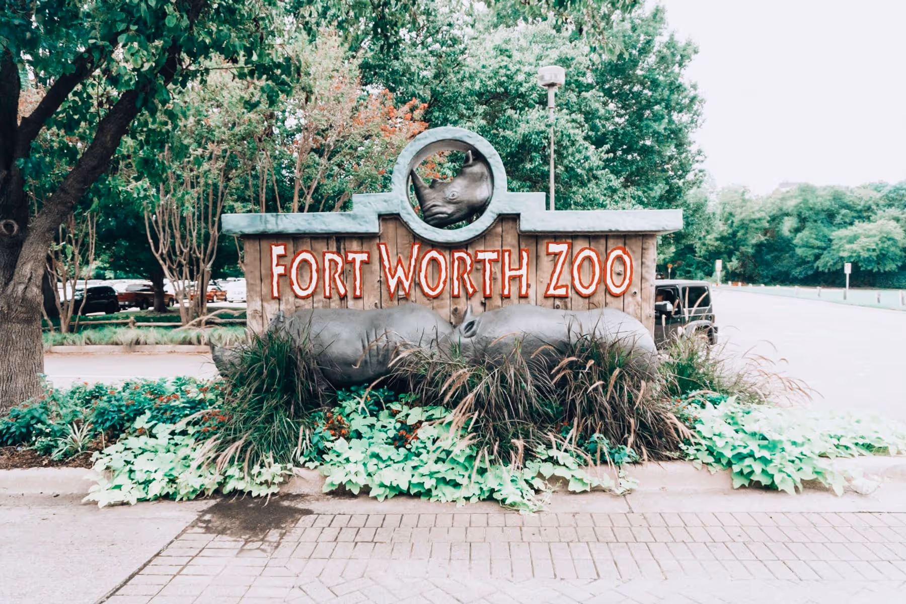 Wooden Fort Worth Zoo entrance sign framed by trees and rhinoceros sculptures