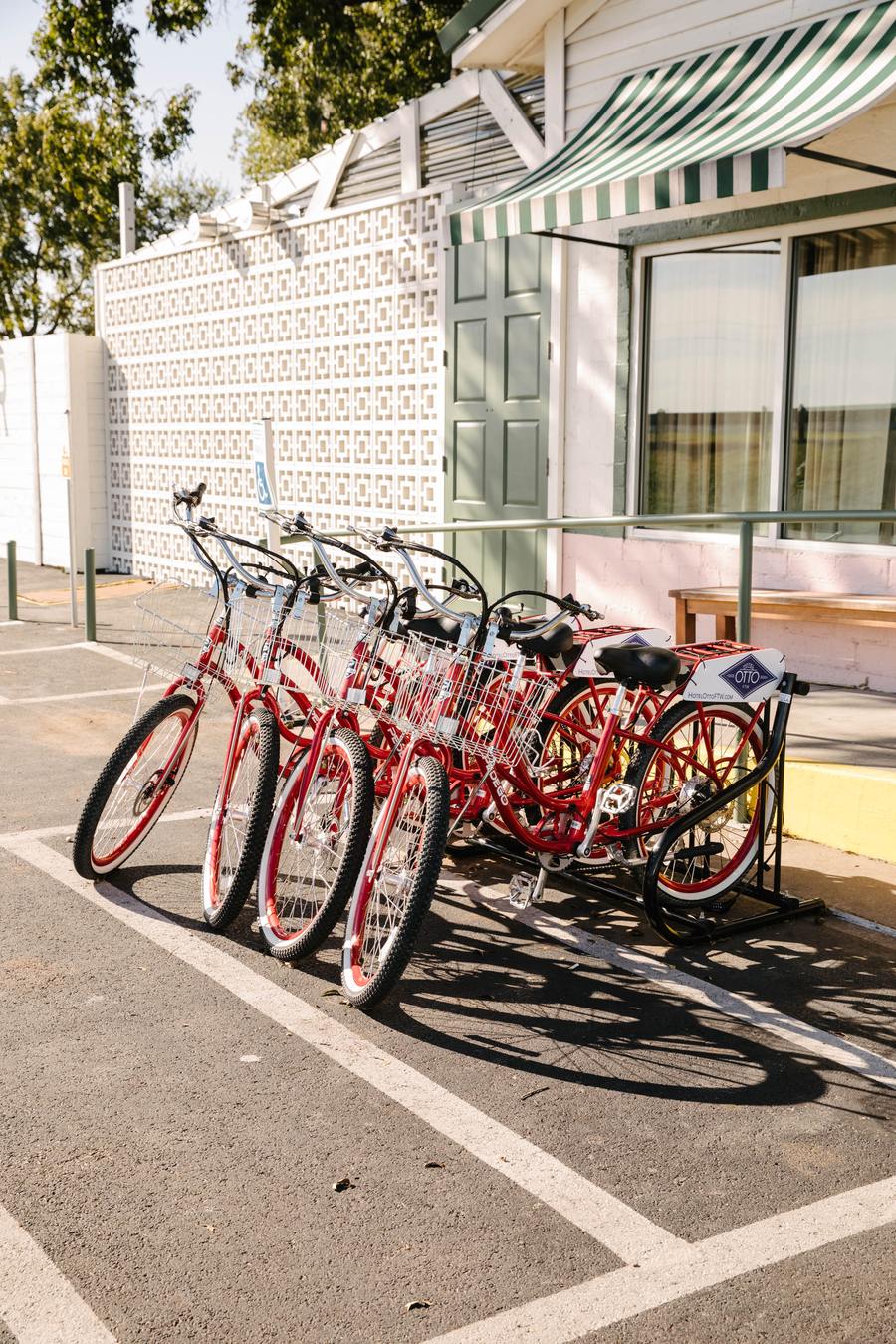 Row of red Hotel Otto cruiser bikes with wire baskets parked in a rack outside the property