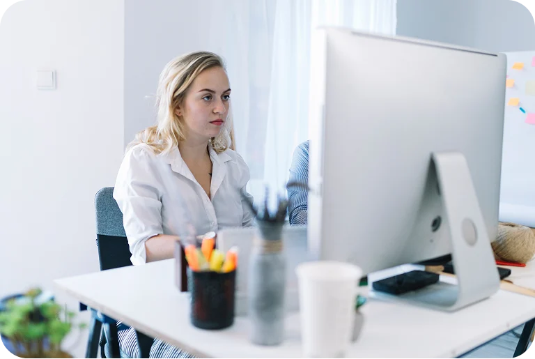 Woman in white shirt focused on a computer screen at a bright modern office desk.
