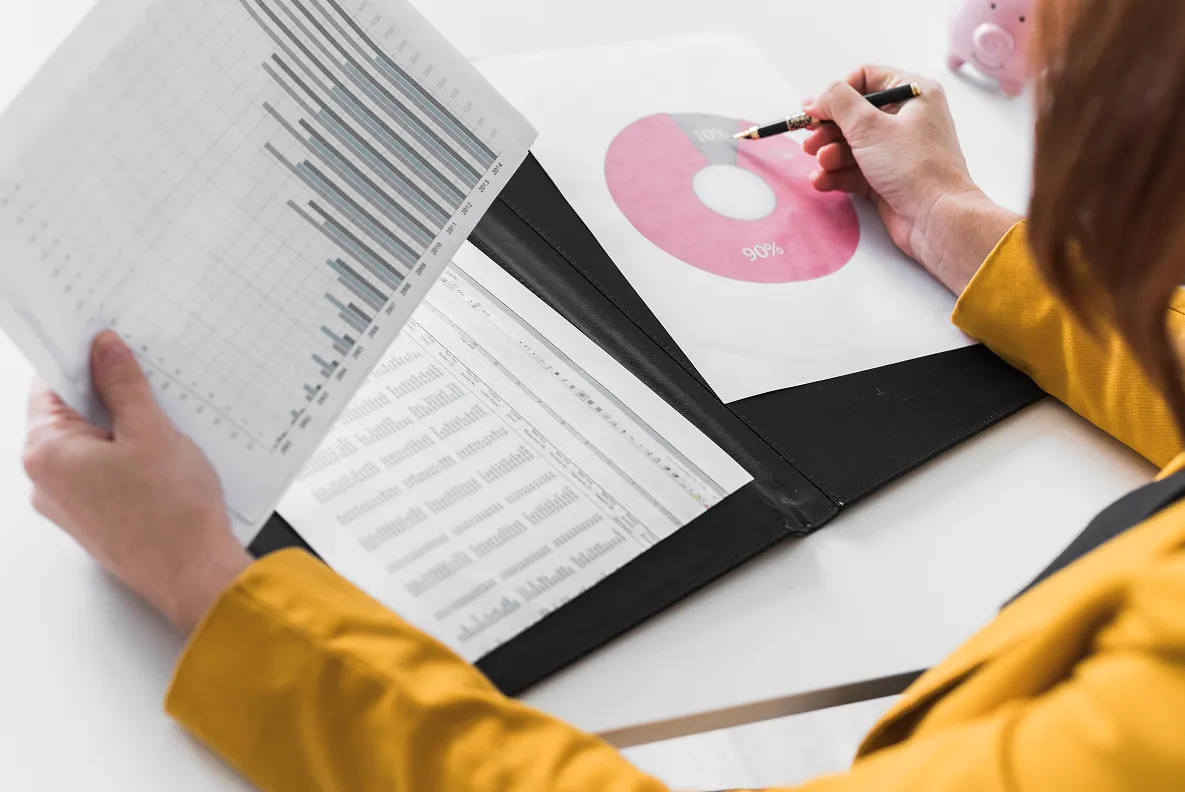 Person in yellow jacket reviewing financial charts including a bar graph and a pink donut chart with percentages.