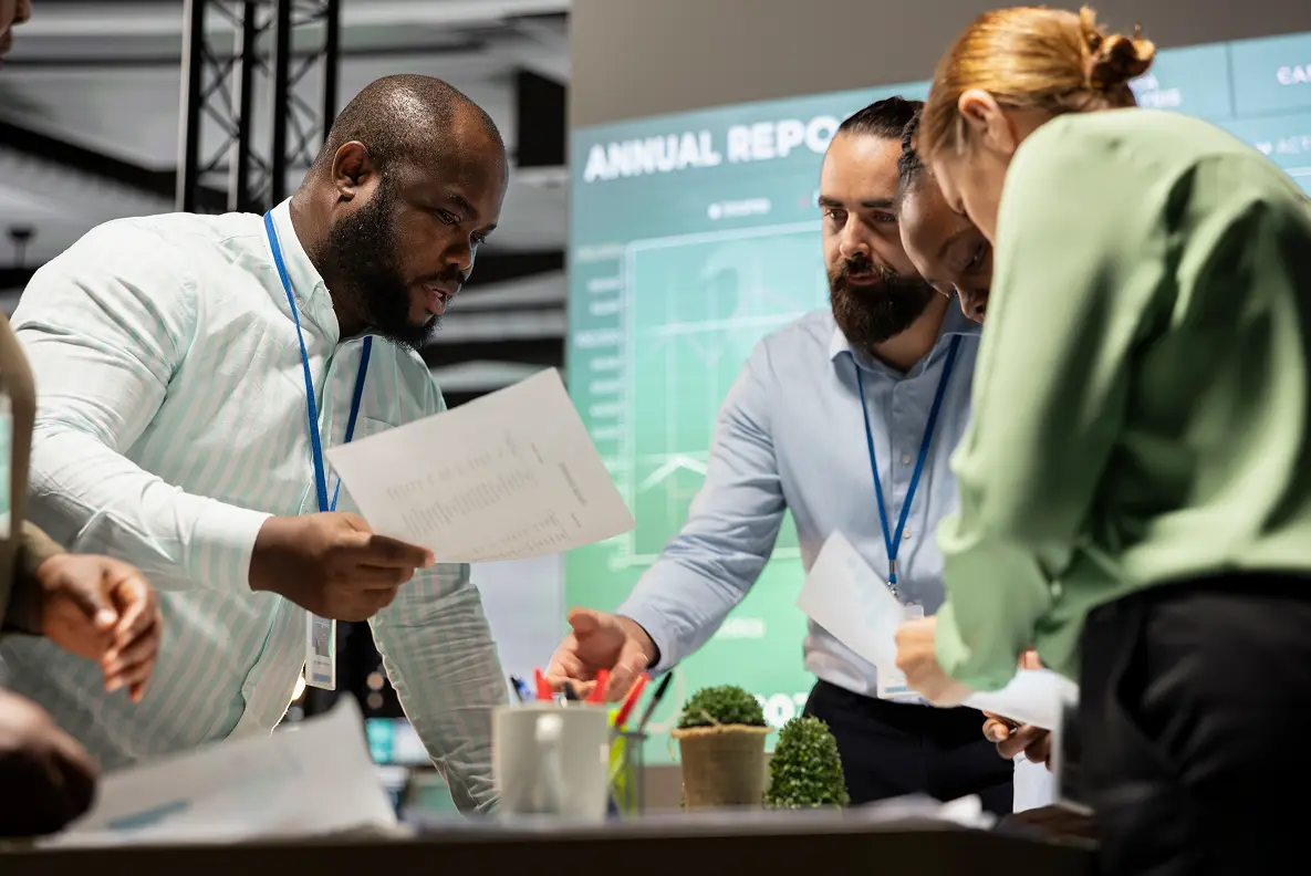 A diverse group of professionals examining documents and discussing an annual report in a modern office.