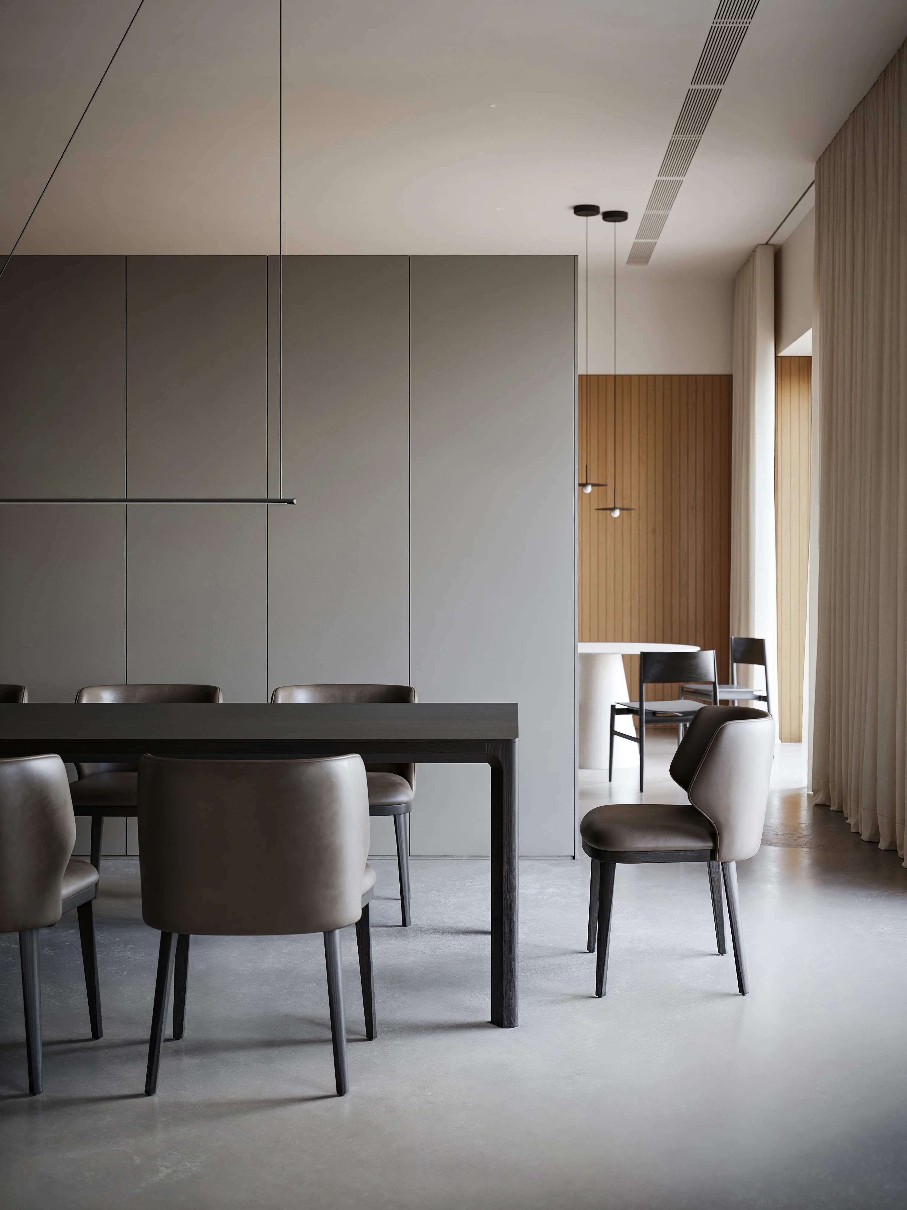 Minimalist dining room with a dark rectangular table and six taupe upholstered chairs on a polished concrete floor.