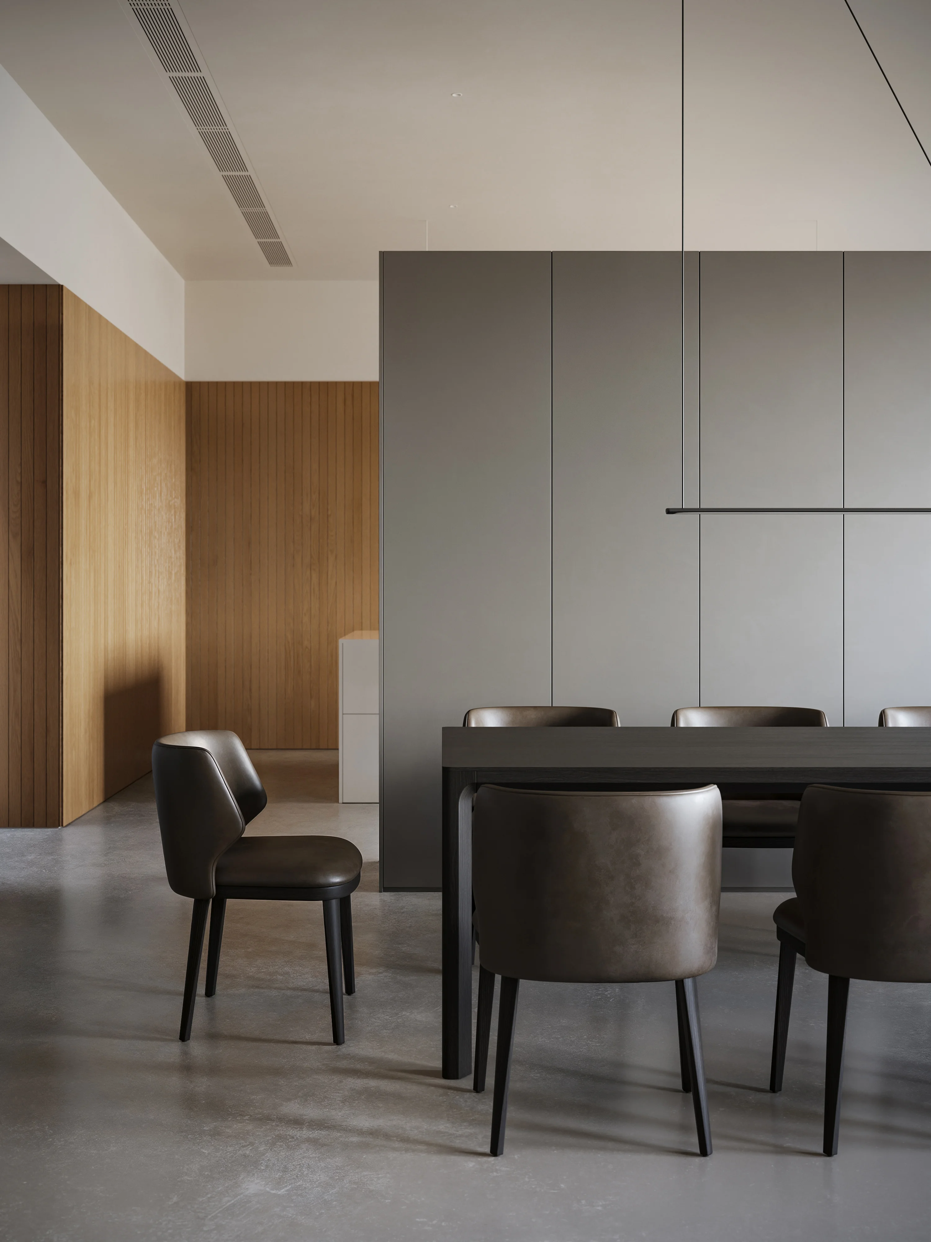 Minimalist dining area with dark brown leather chairs and a black rectangular table, set against gray and wooden paneled walls.
