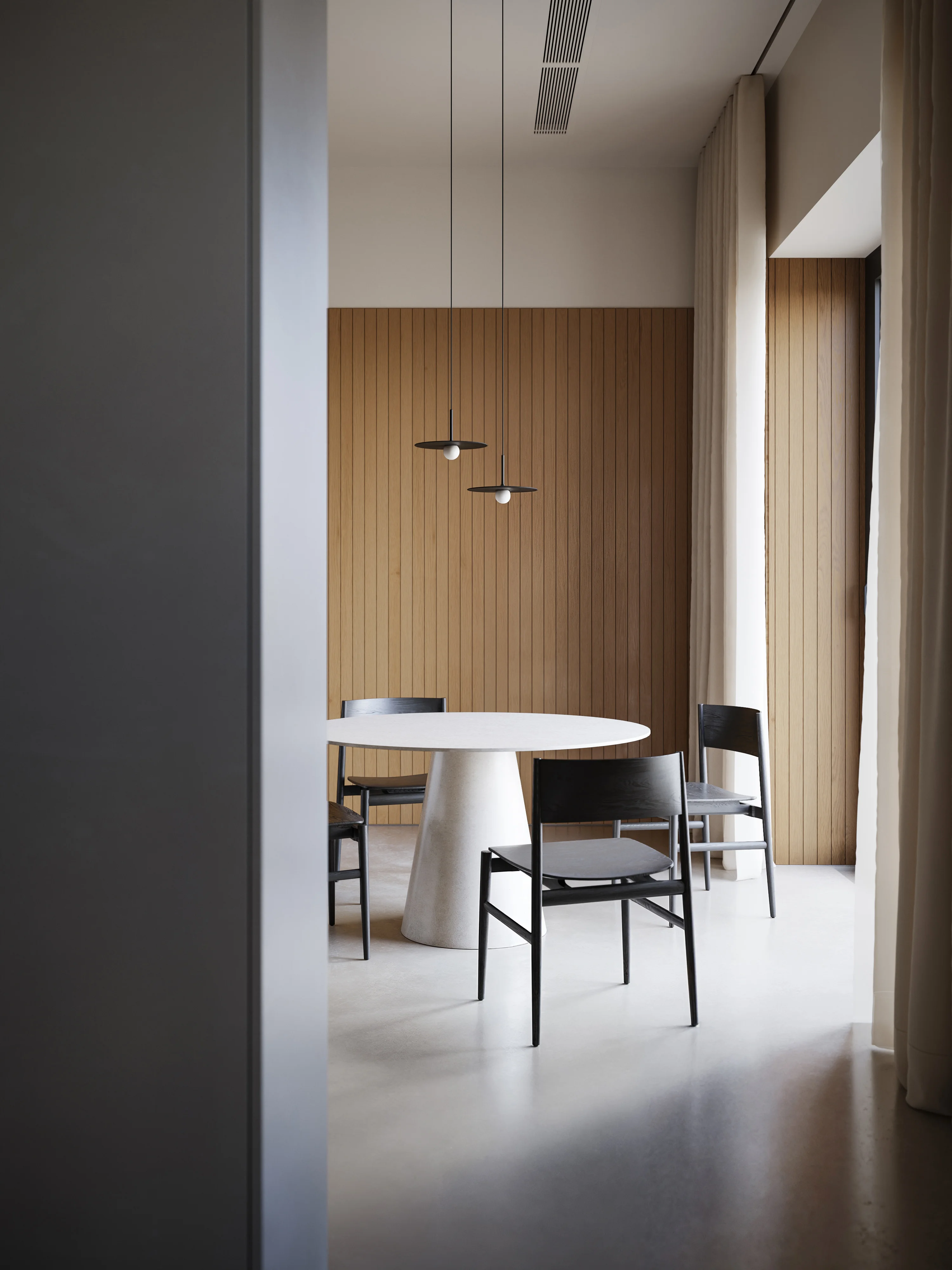 Minimalist dining area with a round white table, four black chairs, wood-paneled wall, and two modern pendant lights.