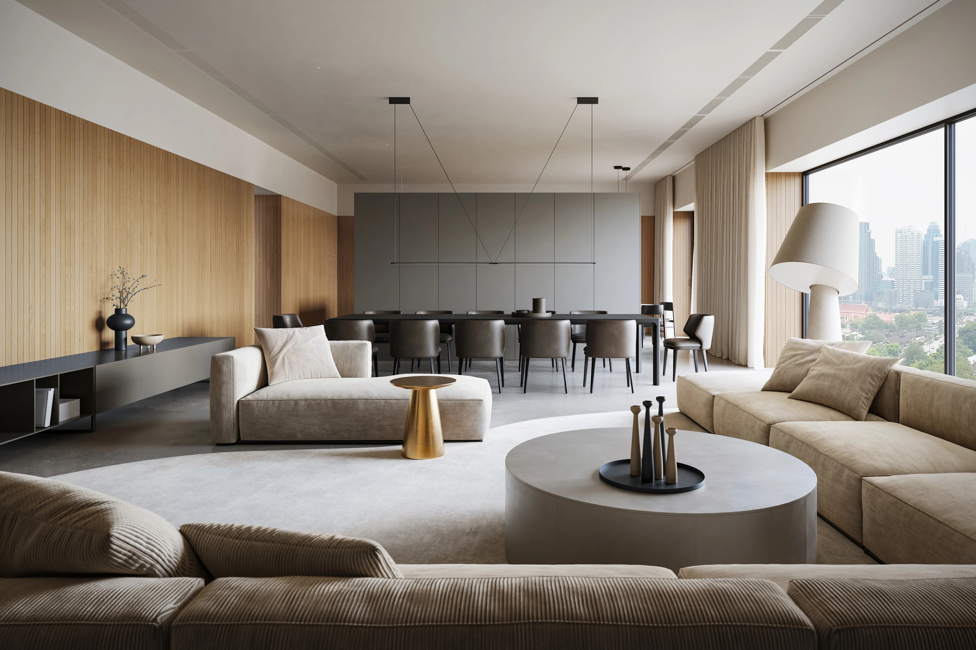 Modern living room with beige sofas, a round coffee table with decorative objects, a gold side table, and a dining area with dark chairs against a gray panel wall.