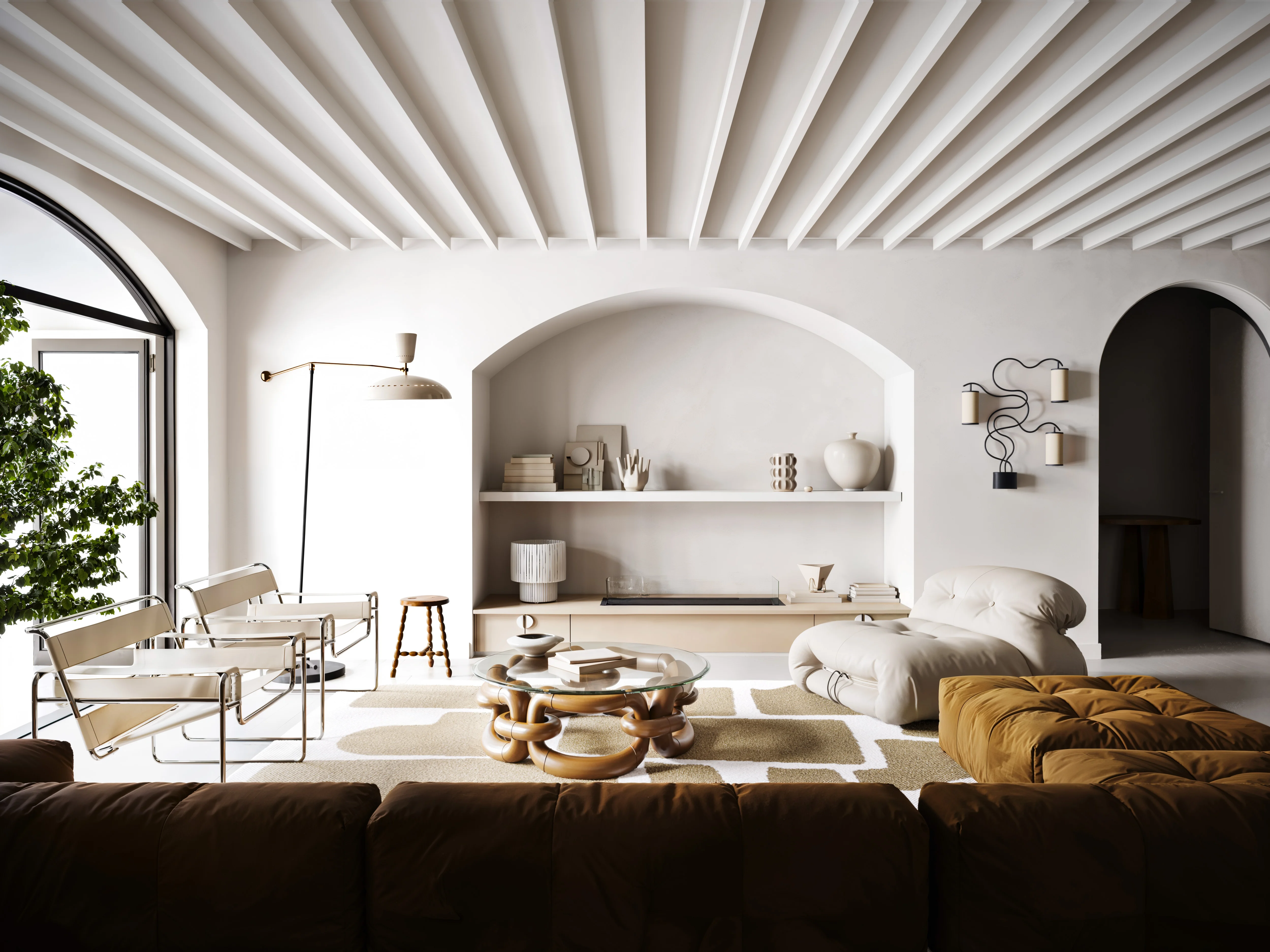 Modern living room with white walls, arched niches, a beige cushioned lounge chair, patterned rug, glass-top coffee table, and large indoor plant by an arched window.