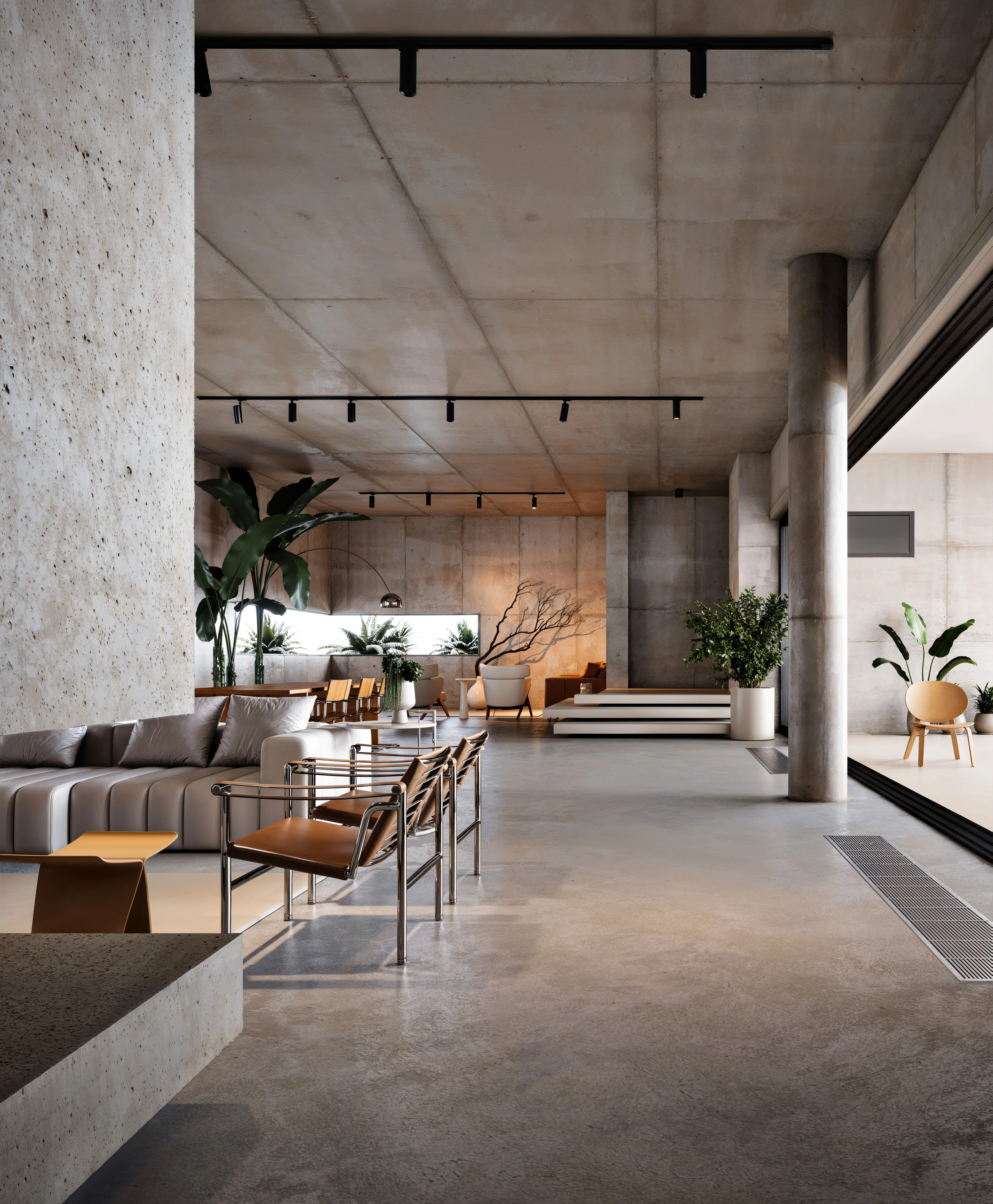 Modern living room with concrete walls and floor, featuring a gray sectional sofa, leather chairs, wooden dining chairs, and various indoor plants.