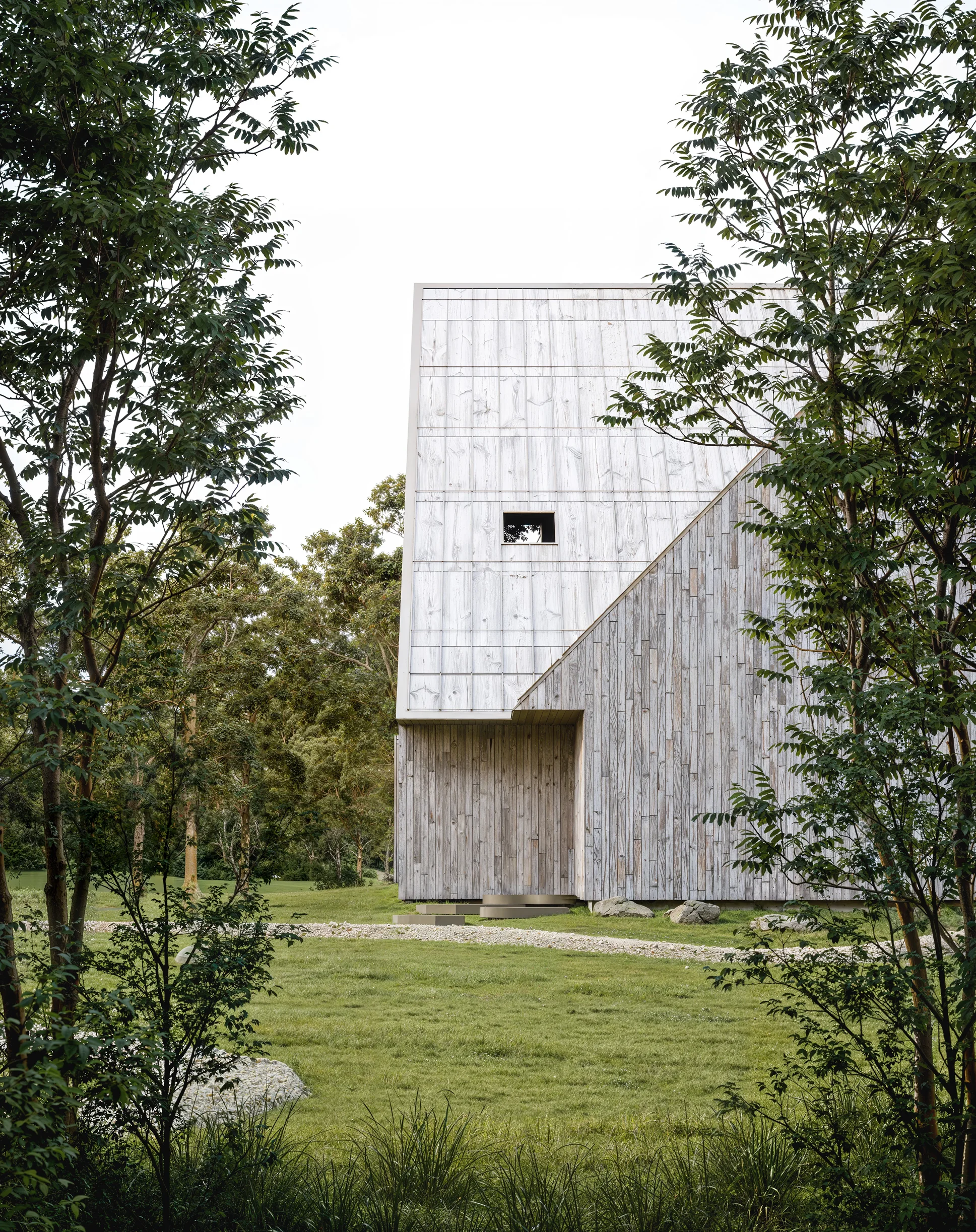 Modern wooden house with diagonal roof and small window, surrounded by trees and grassy lawn.