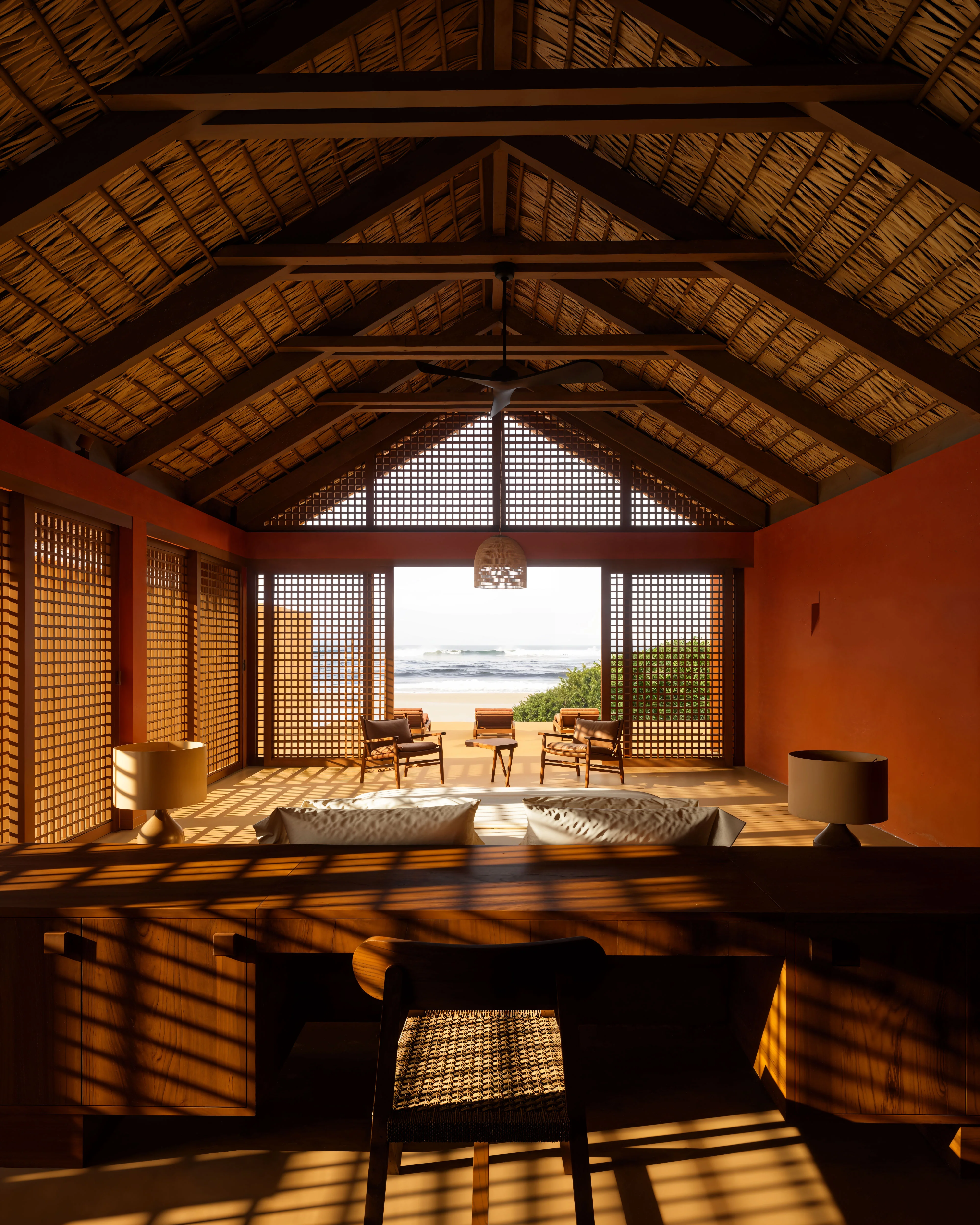 Interior of a tropical wooden pavilion with woven ceiling, lattice walls, and chairs facing a beach view with ocean waves.