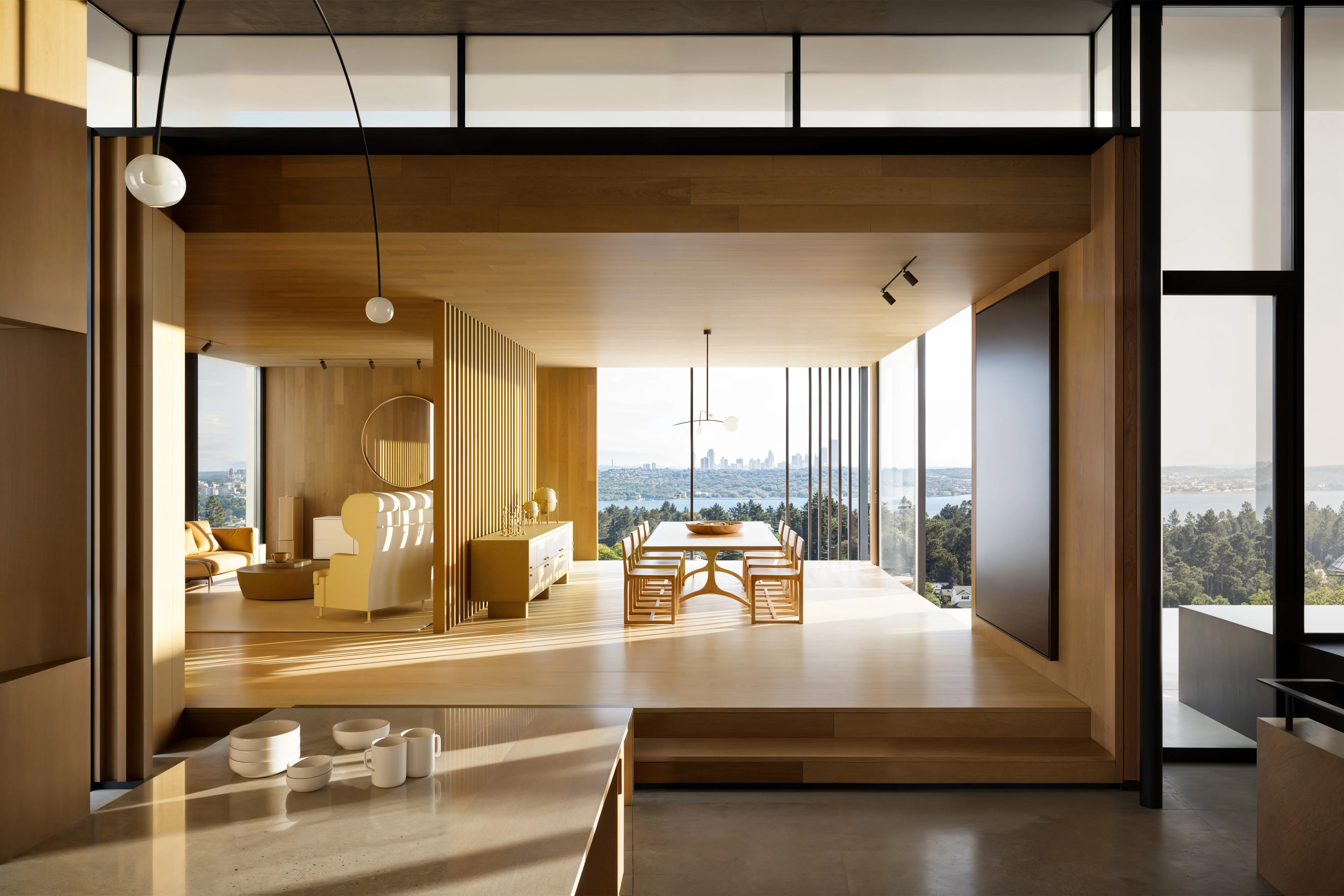 Modern open-concept dining and living area with wood paneling, large windows offering city and water views, and minimalist furniture.