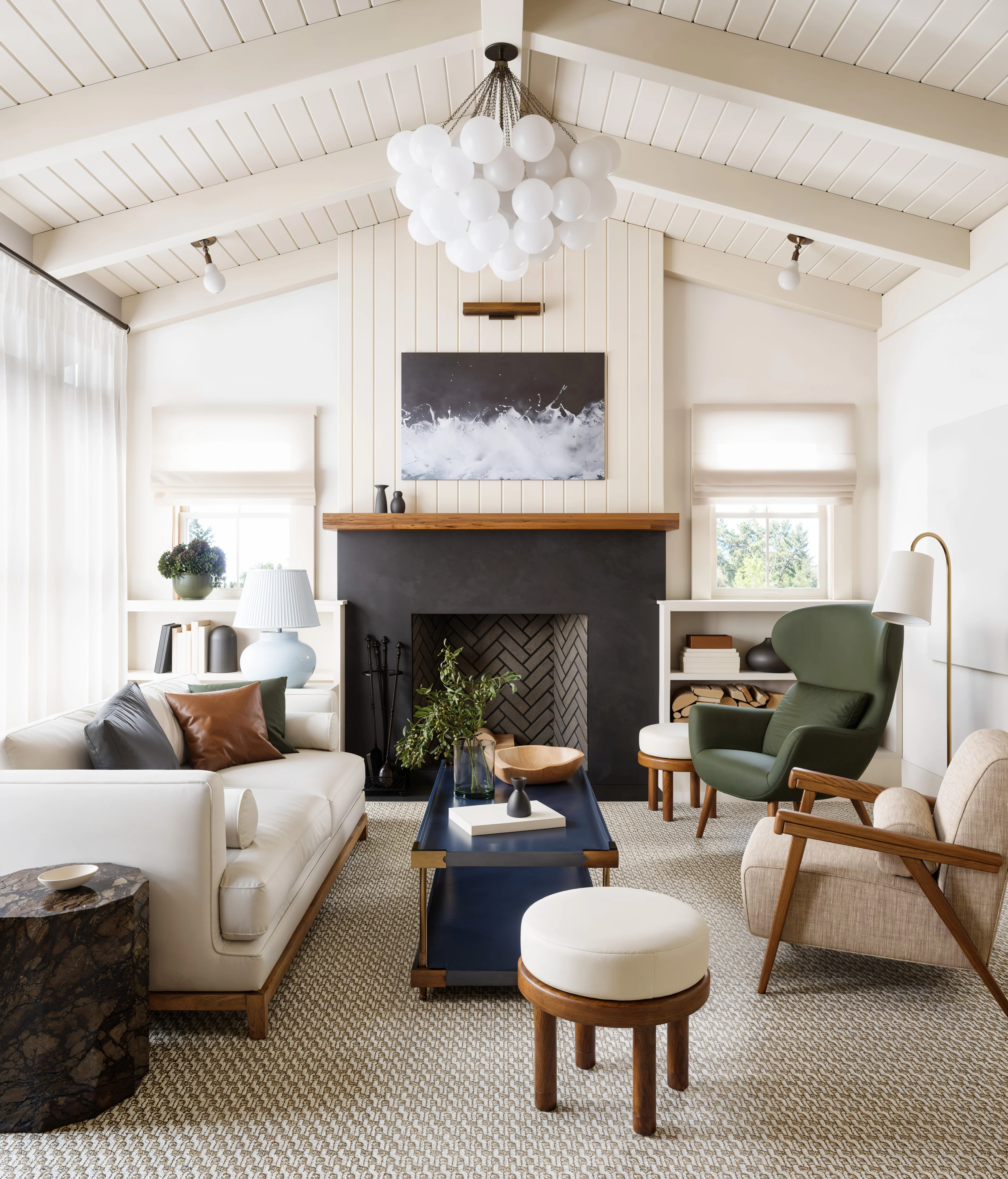 Modern living room with vaulted ceiling, cluster chandelier, cream sofa, green armchair, black fireplace, and blue coffee table.