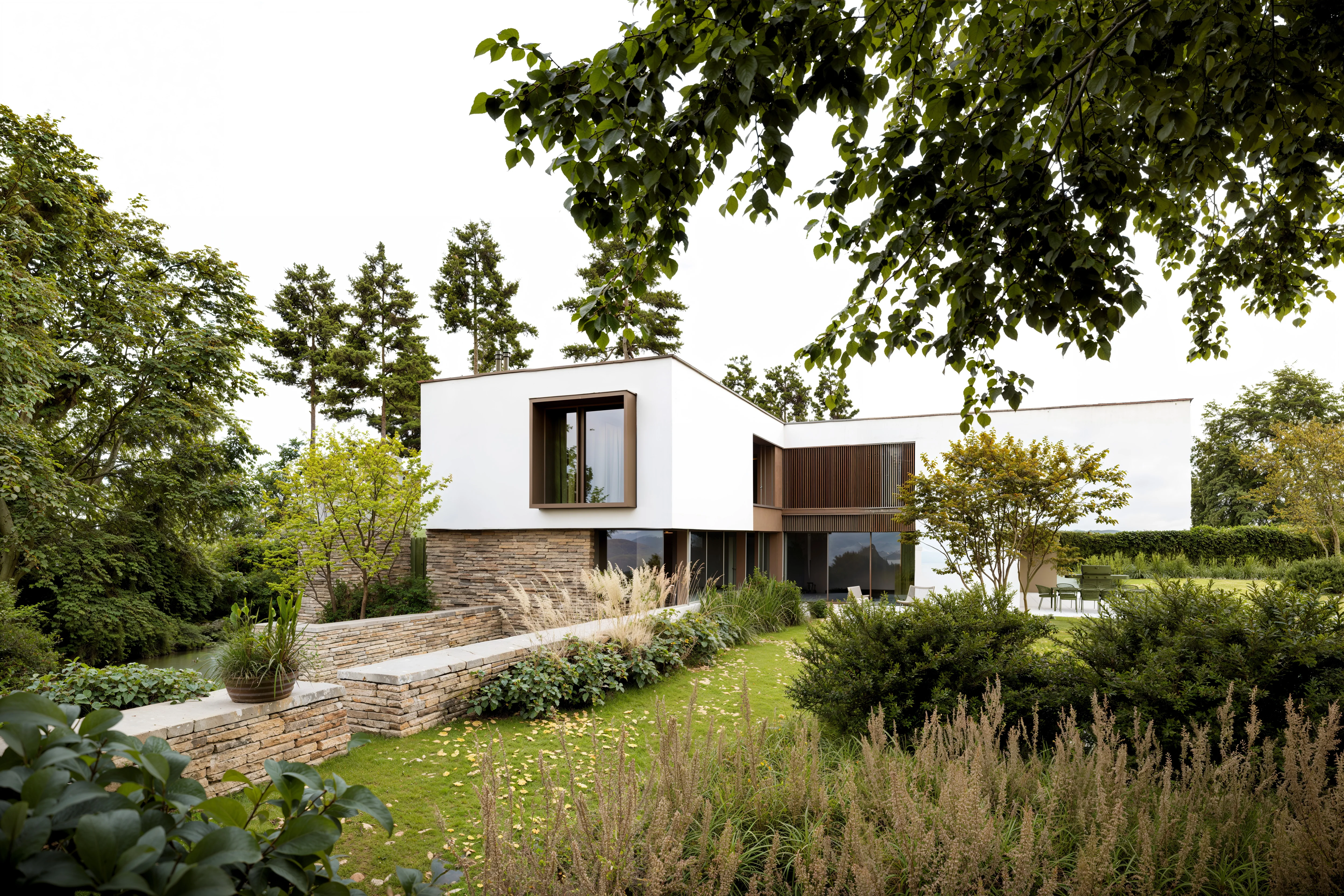 Modern two-story house with white and stone exterior surrounded by lush green trees and landscaped garden.
