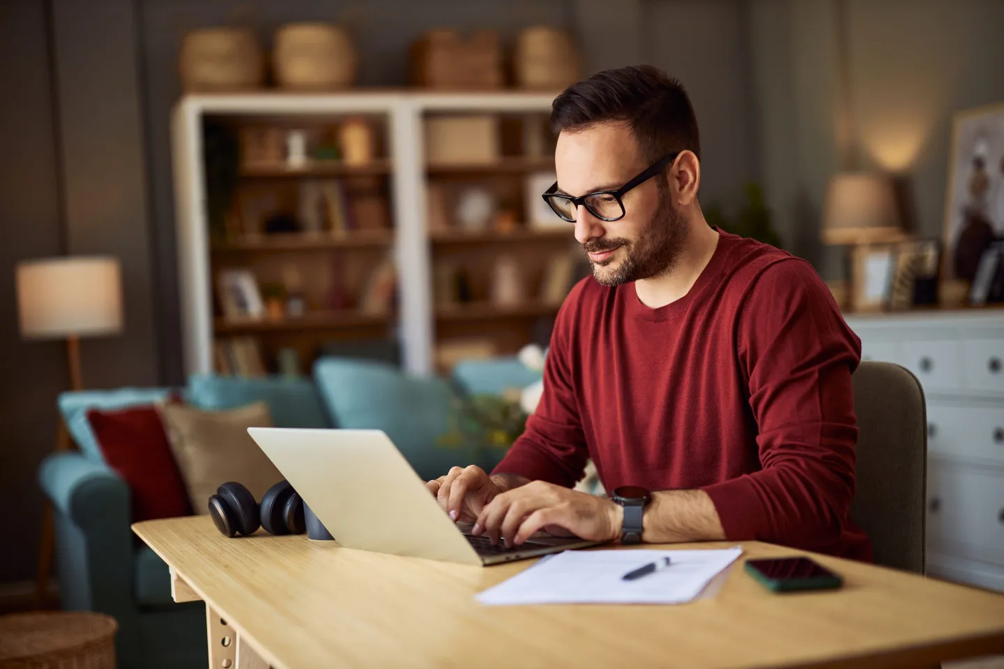 Man with glasses and red sweater typing on laptop