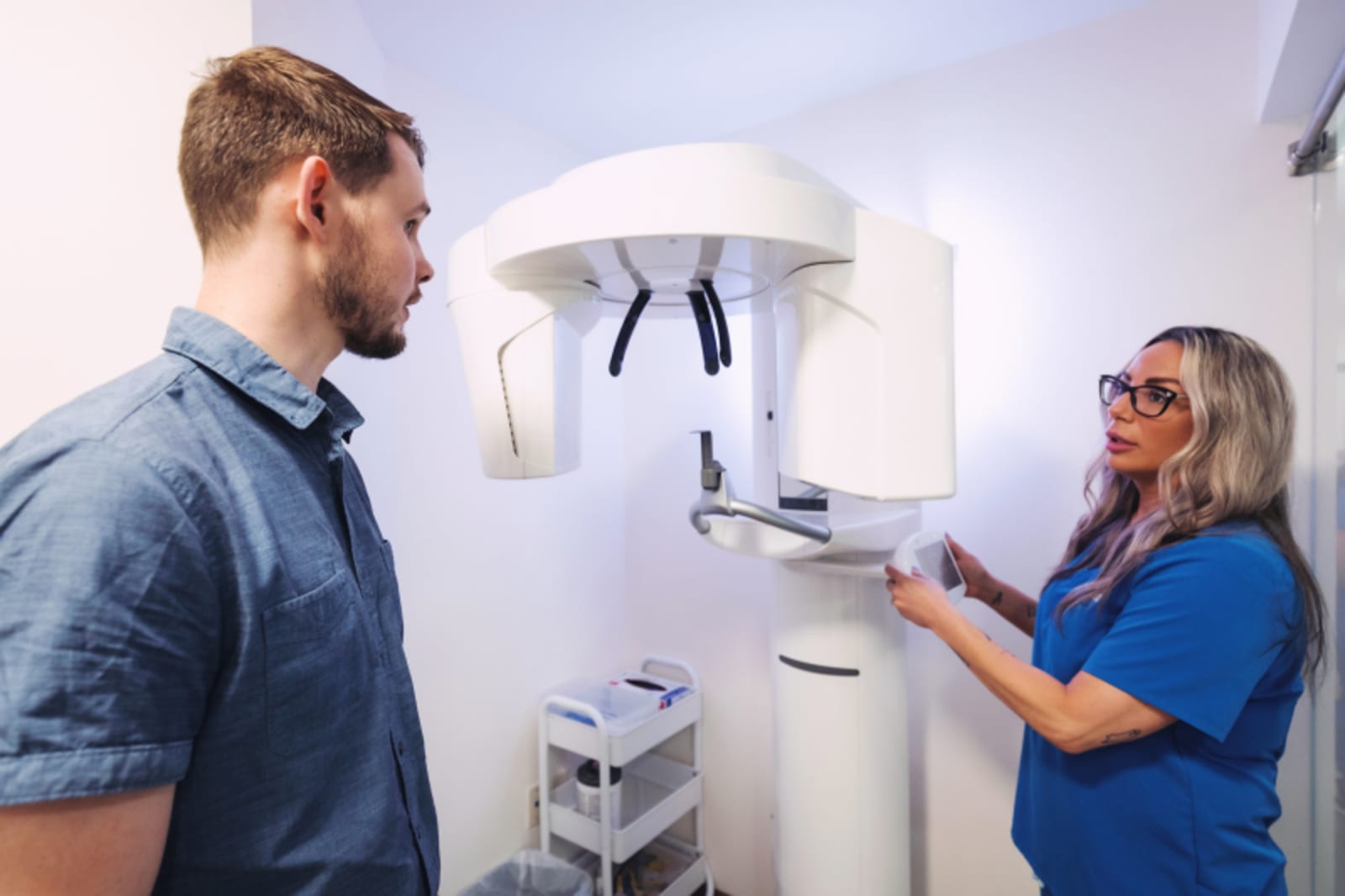 Dentist showing dental implant X-ray to male patient in office treatment room.