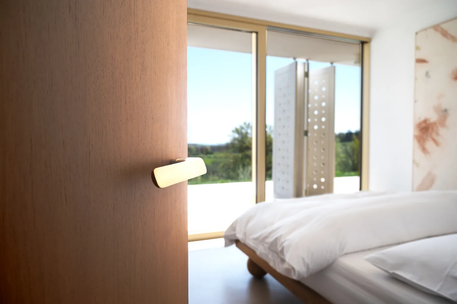 Master bedroom with floor-to-ceiling windows, wood veneer door with M&T Minimal 2.0 ergonomic door handle in matte gold-like finish.