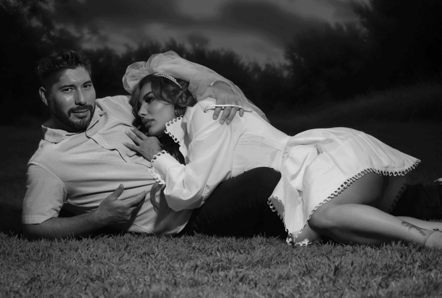 Romantic black-and-white wedding photo of a bride in a short white dress and veil lying on the grass with her groom in a park at night in Southern Highlands, Las Vegas.