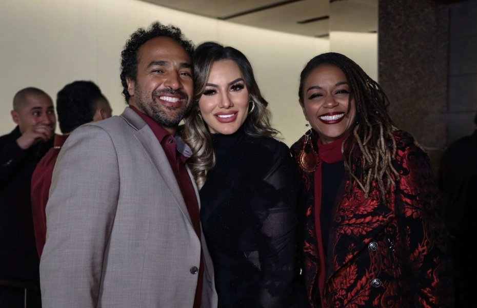 Venessa Patino smiles while posing with two guests, a man in a blazer and a woman in a red patterned jacket