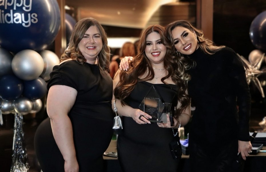 Venessa Patino poses with two women in black dresses, one holding an award plaque, in front of holiday balloons at Adam S. Kutner’s Holiday Party.