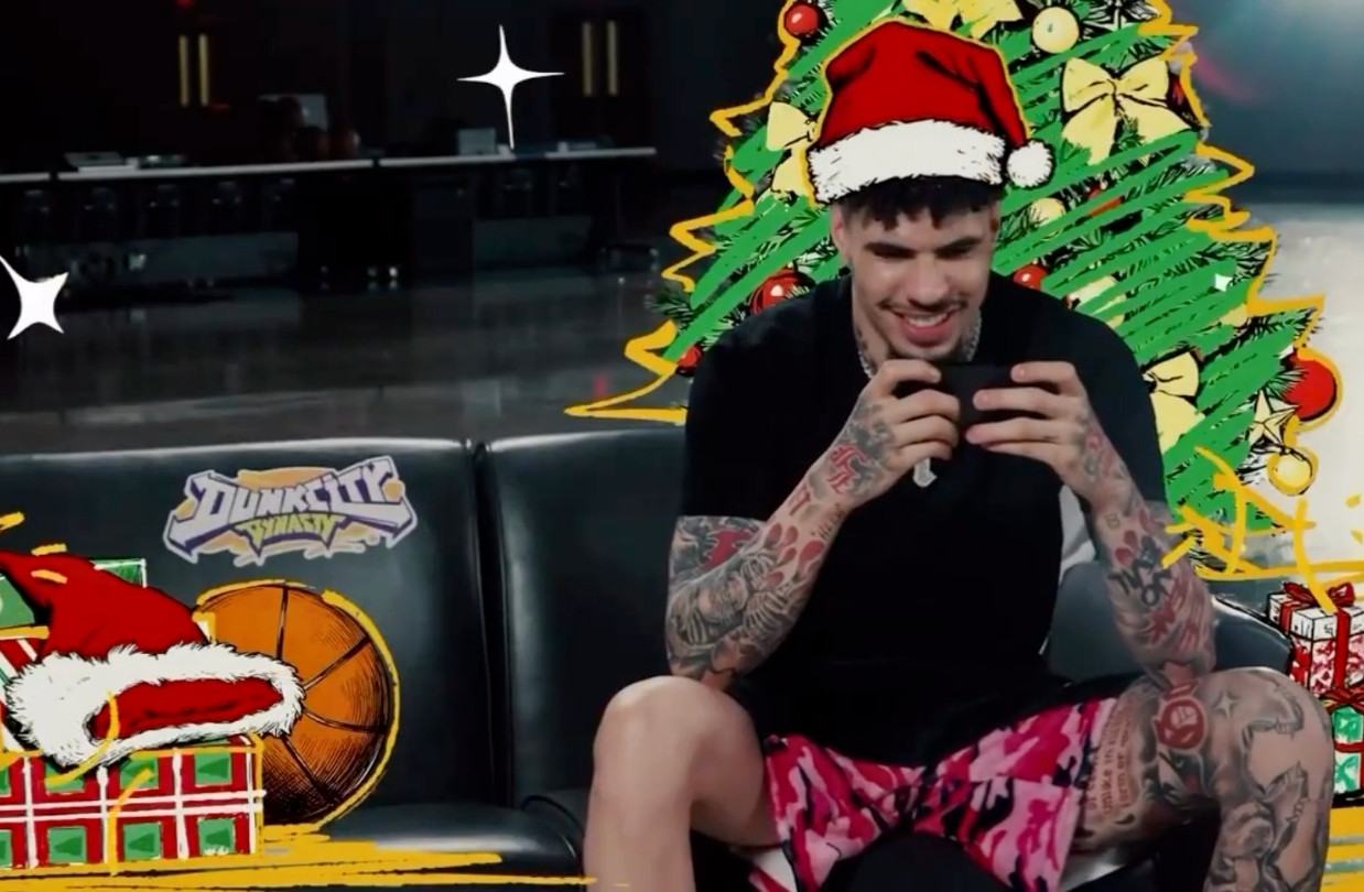 LaMelo Ball sits on a couch playing Dunk City Dynasty, wearing a Santa hat and surrounded by illustrated holiday elements.