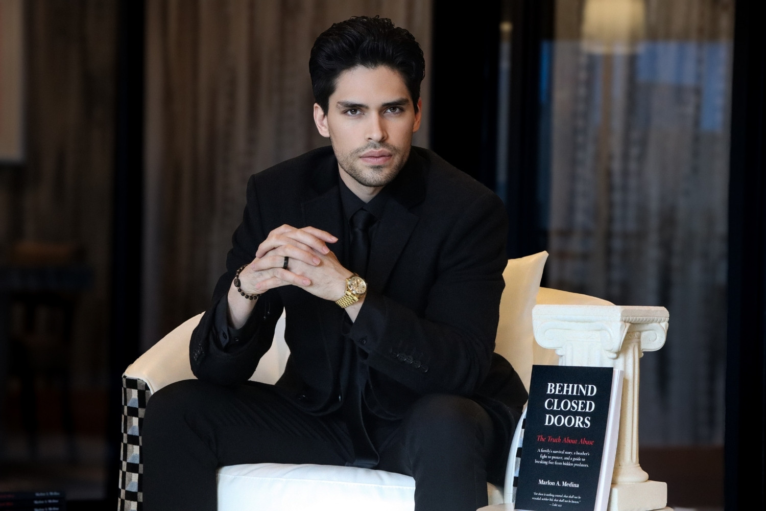Author seated with copy of Behind Closed Doors in a quiet interior setting