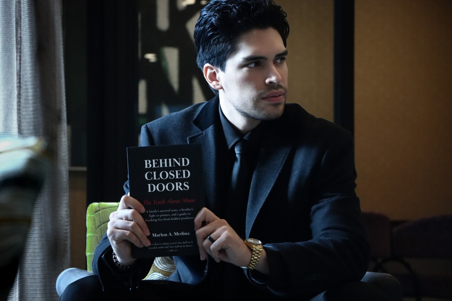 Author seated indoors holding Behind Closed Doors in natural light