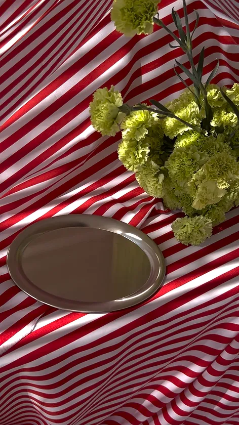 Silver oval tray placed on a red and white striped fabric background next to a bunch of green carnations.