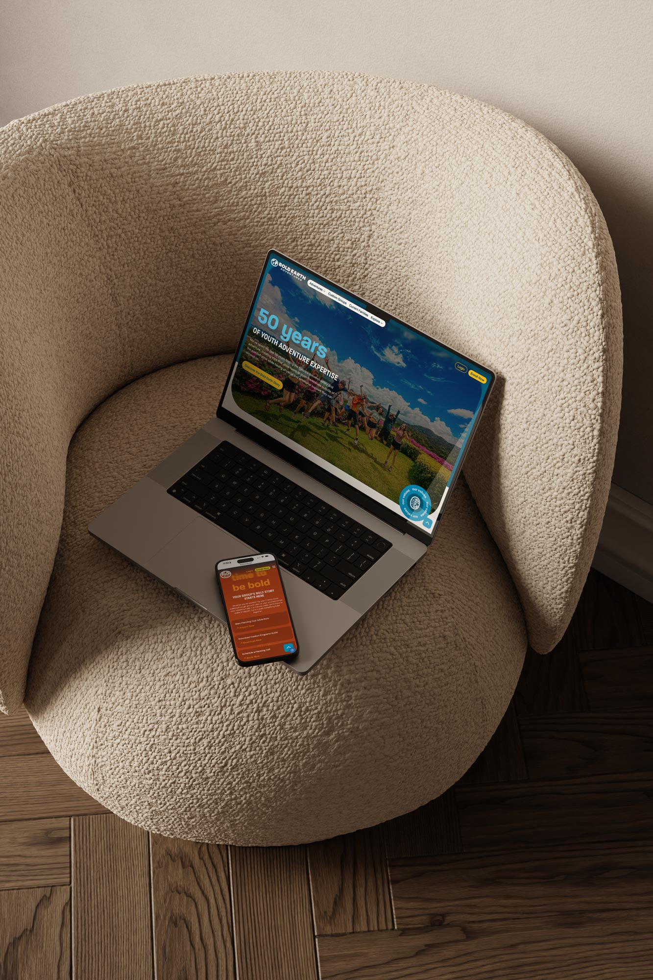 Laptop and smartphone displaying the Bold Earth website, placed on a textured armchair.
