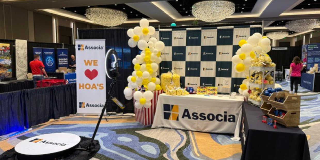 Associa-branded trade show booth featuring a photo booth setup, balloon displays, promotional games, giveaways, and a “We Love HOA’s” banner at a community association industry event.
