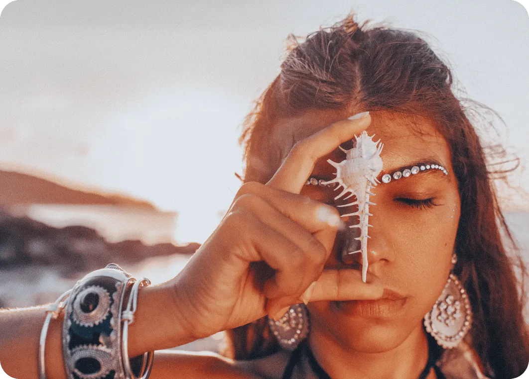 Eine junge Frau im Boho Stil mit einer Muschel vor dem Gesicht