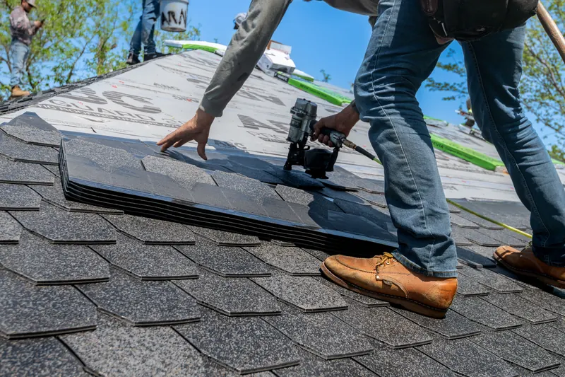 Roofer installing architectural asphalt shingles over new underlayment during a roof replacement