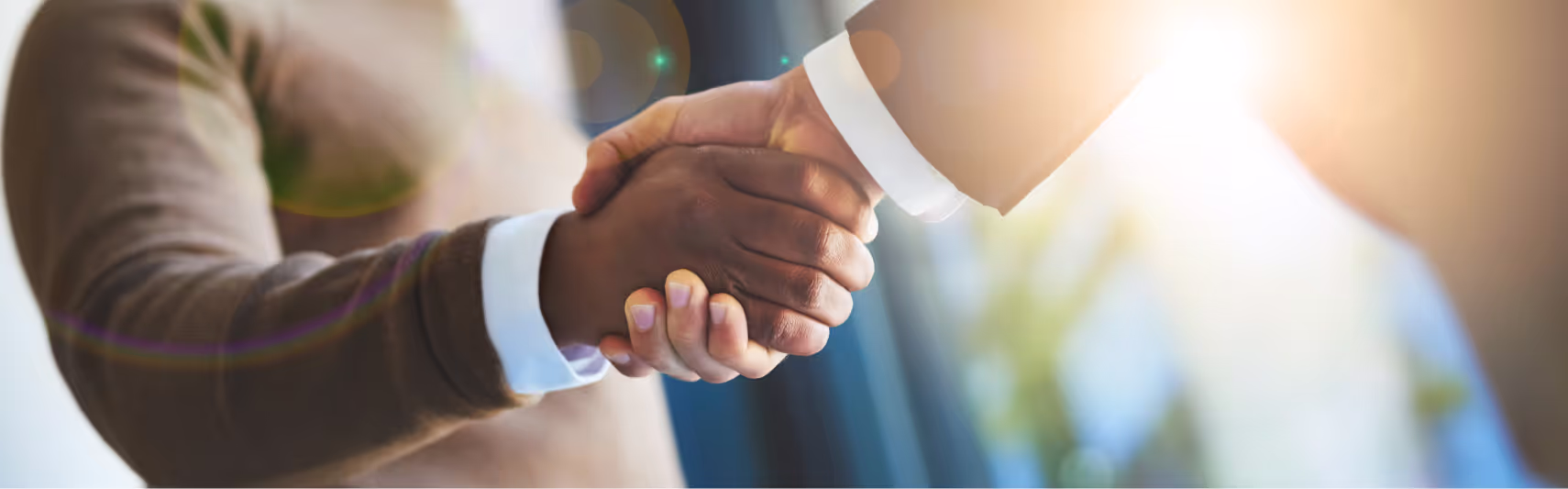 Two people shaking hands in a business setting with sunlight filtering in the background.