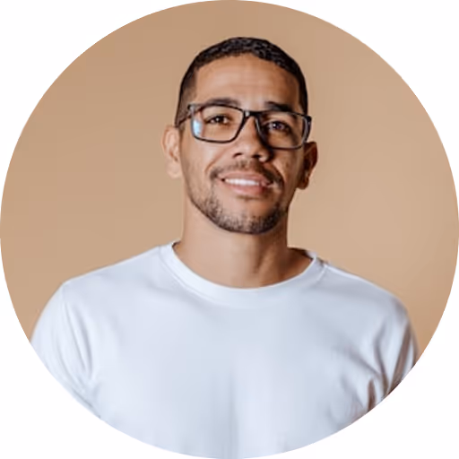 Smiling man with short black hair, glasses, and a white shirt against a beige background.