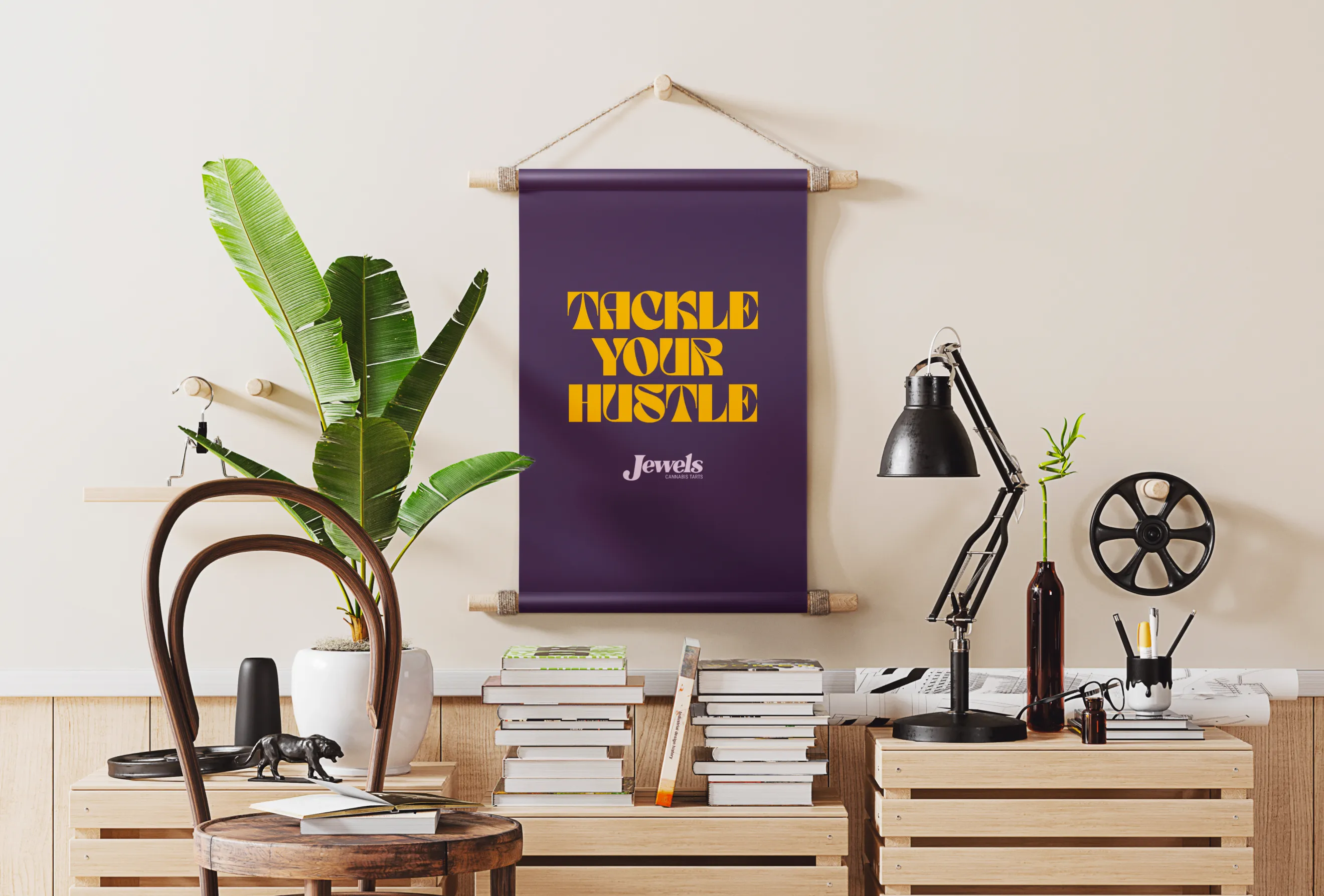 Deep purple poster with the orange phrase “TACKLE YOUR HUSTLE” and the white Jewels logo hanging above books and a desk lamp.