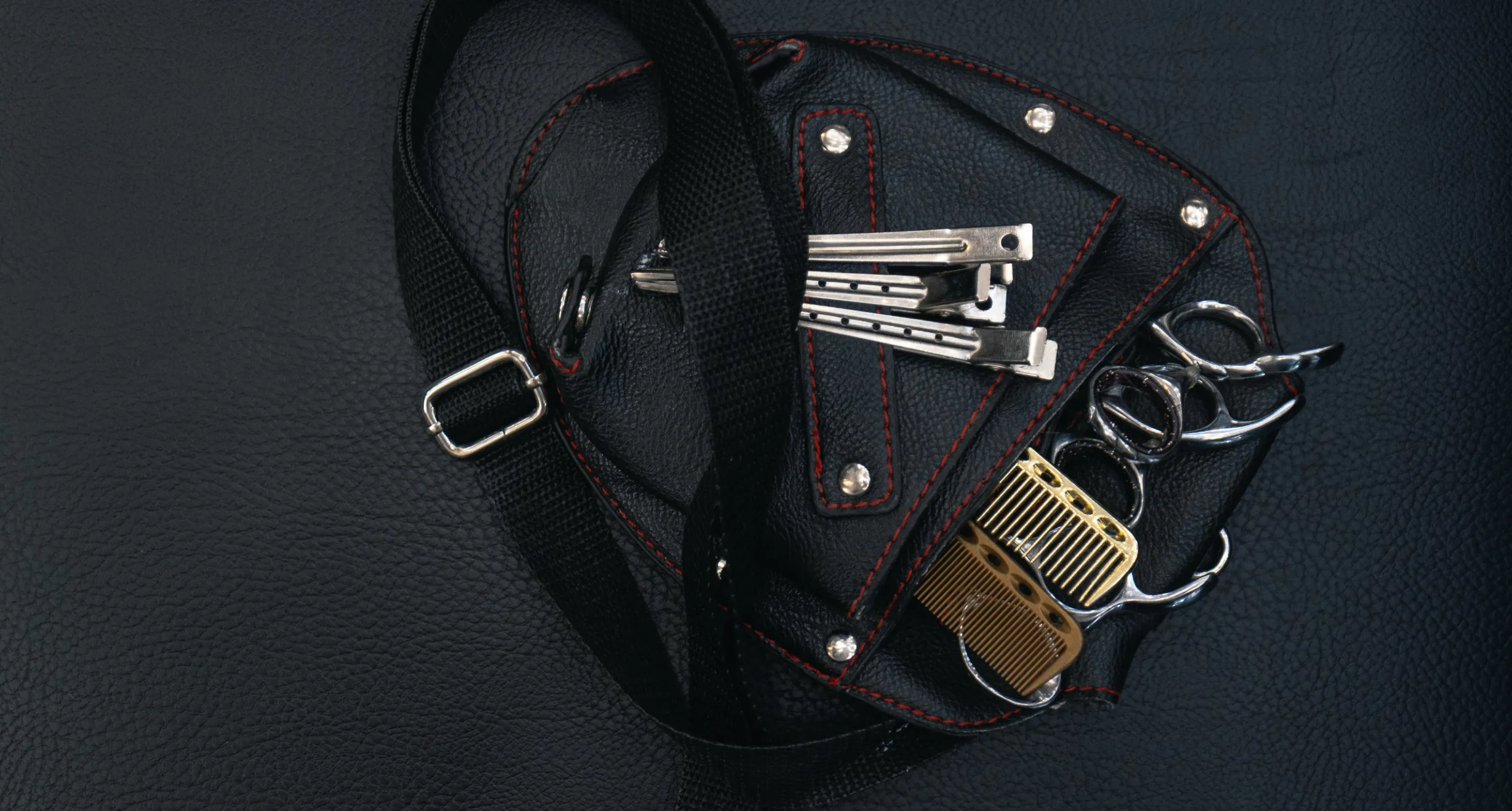 Premium black leather barber tool pouch featuring styling clips, shears, combs, and red stitching details.