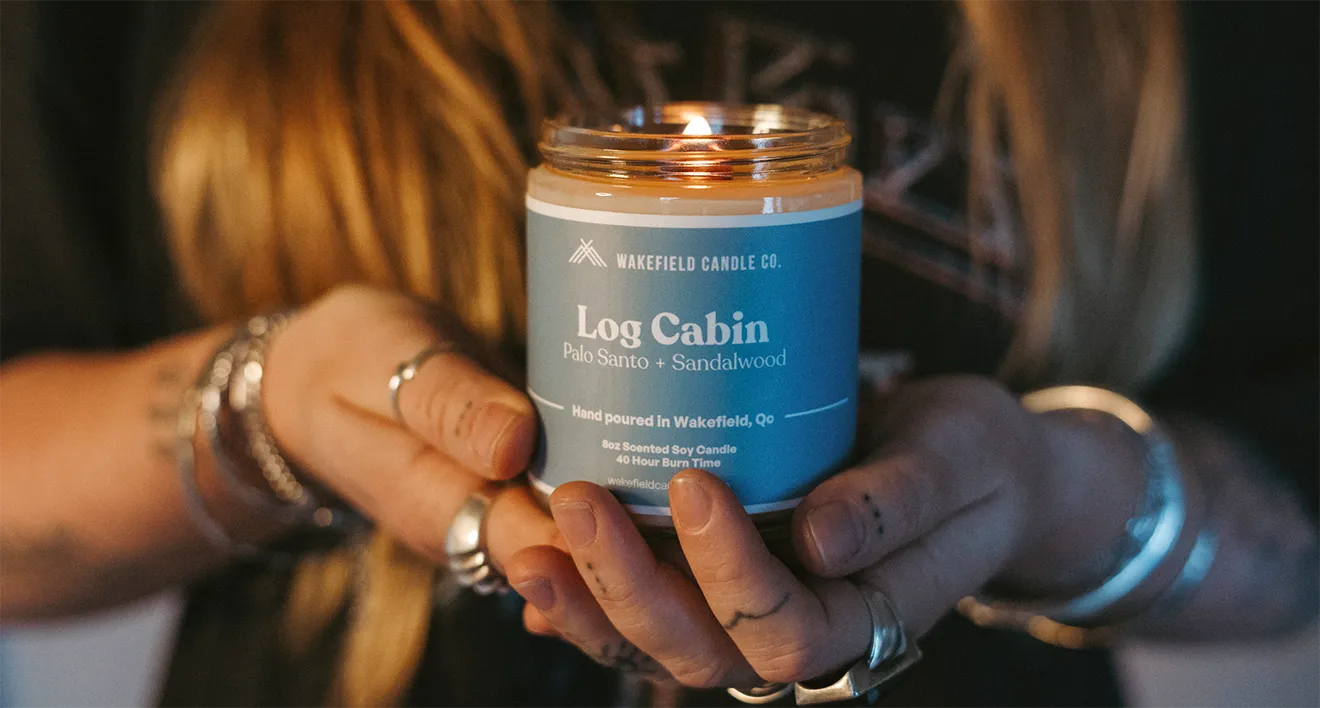 Wakefield Candle Co. owner holding the Log Cabin soy candle in a moody lifestyle photograph.