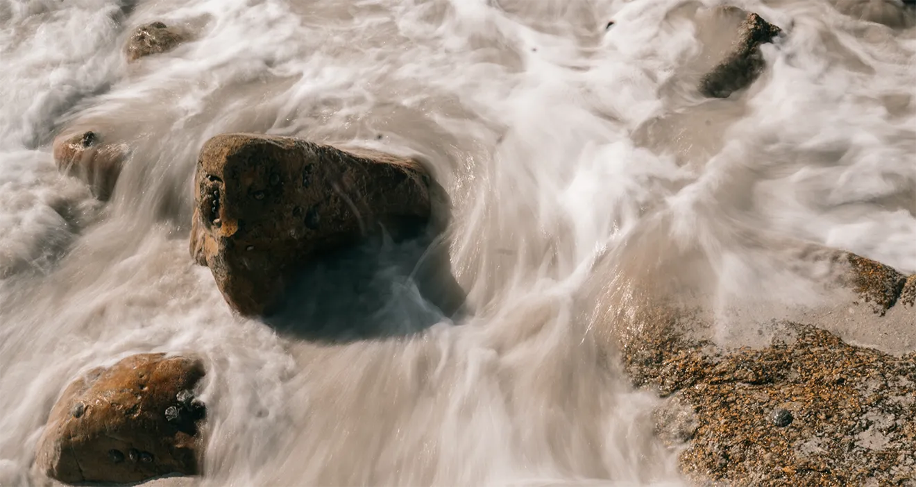Long-exposure photograph of flowing river water over smooth stones representing a calming natural wellness aesthetic.