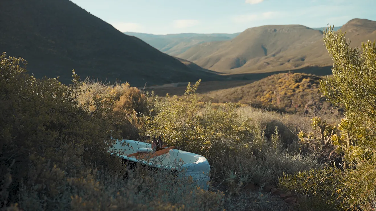 Outdoor bathtub with amber apothecary bottles overlooking a sunlit mountain landscape, representing luxury wellness.