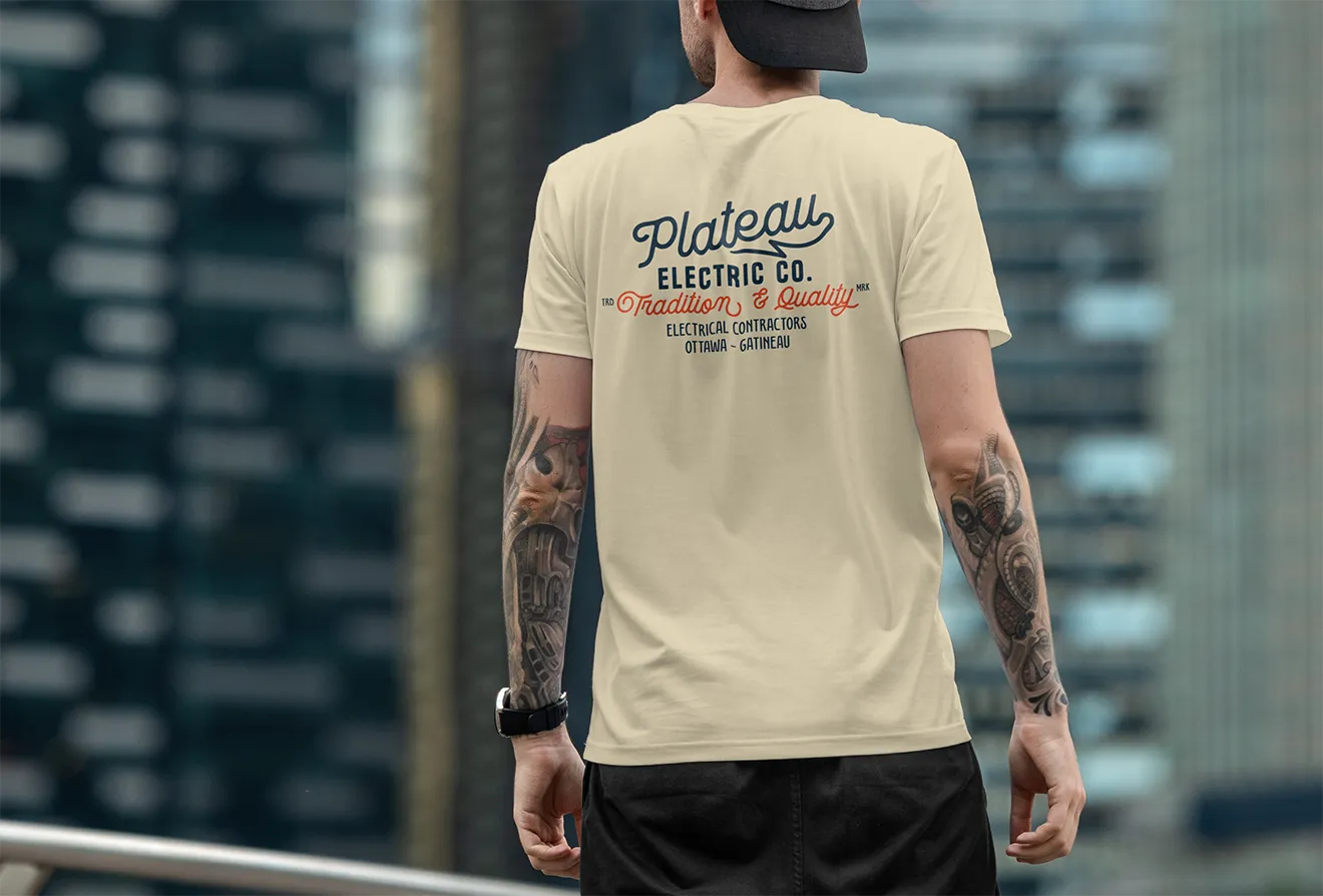Plateau Electric Co. apparel mockup featuring a cream t-shirt with oversized electrical contractor badge graphic.