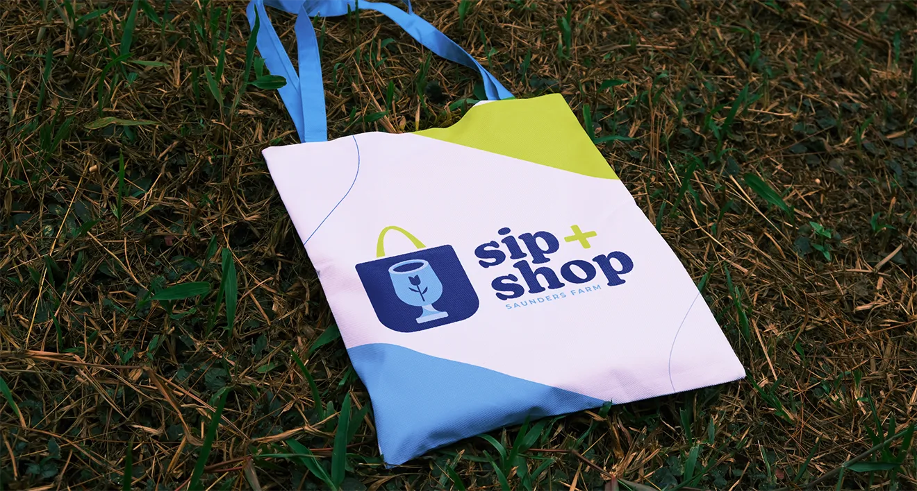 Saunders Farm Sip + Shop tote bag featuring seasonal event branding and illustrated shopping icon.