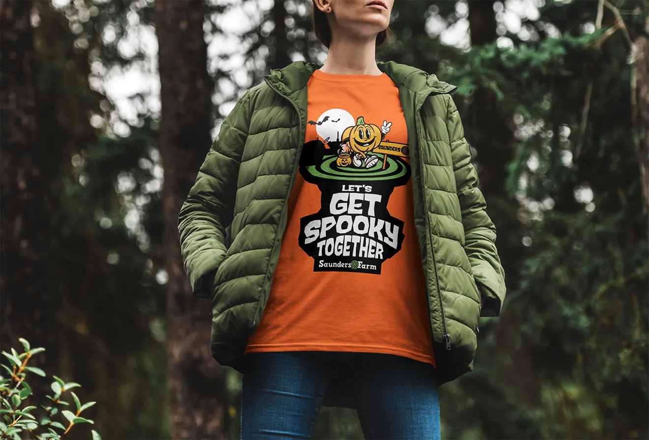 Person wearing an orange Let's Get Spooky Together pumpkin tee, designed for Saunders Farm by Hovski Studio.