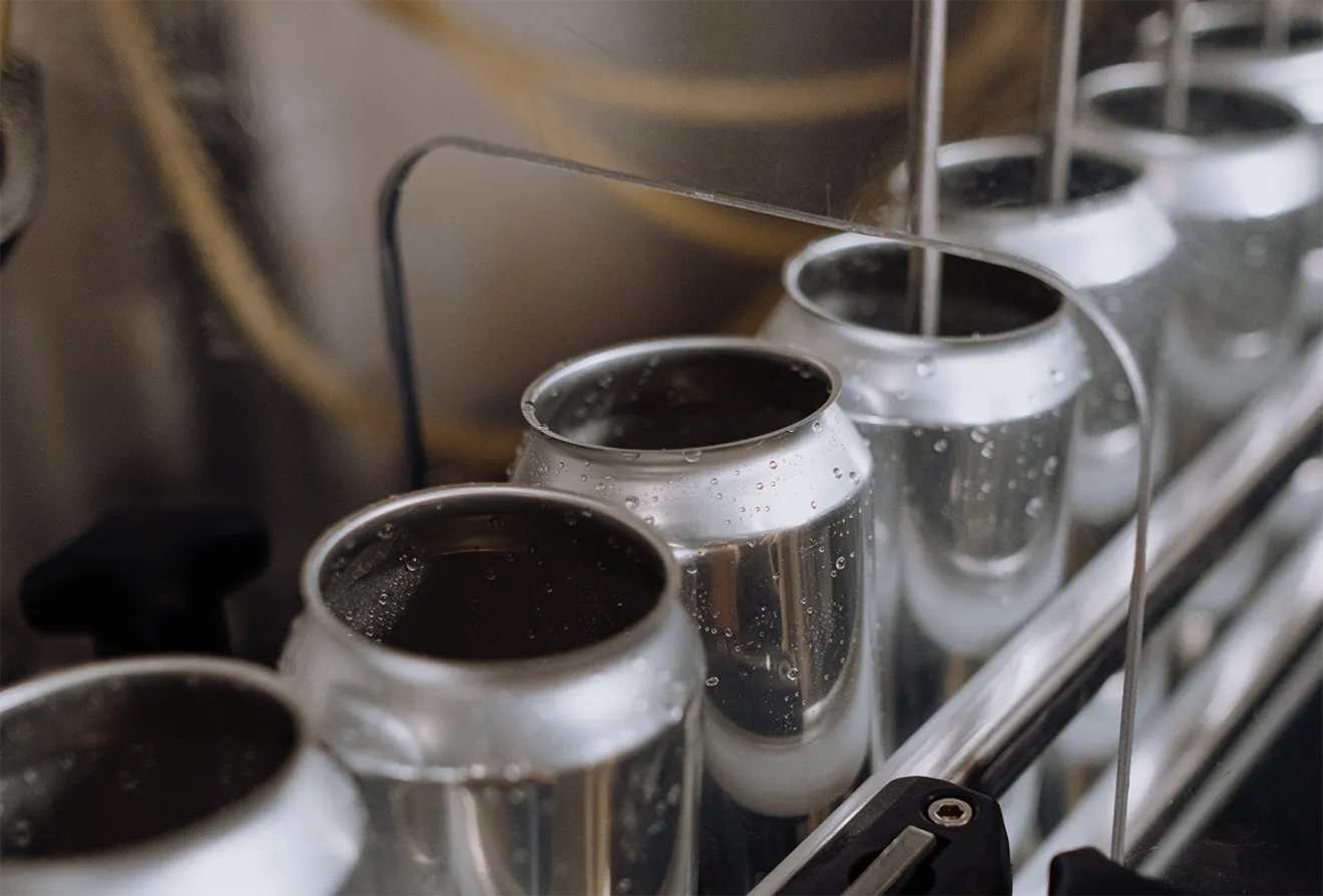 High-angle close-up of aluminum cider cans being filled on a stainless steel conveyor system.