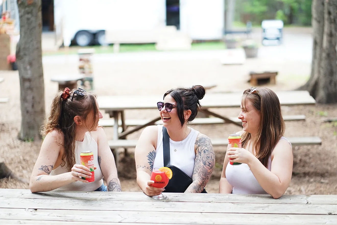 Candid photography by Julie Sproulie of three women enjoying Saunders Cider outdoors at Saunders Farm.