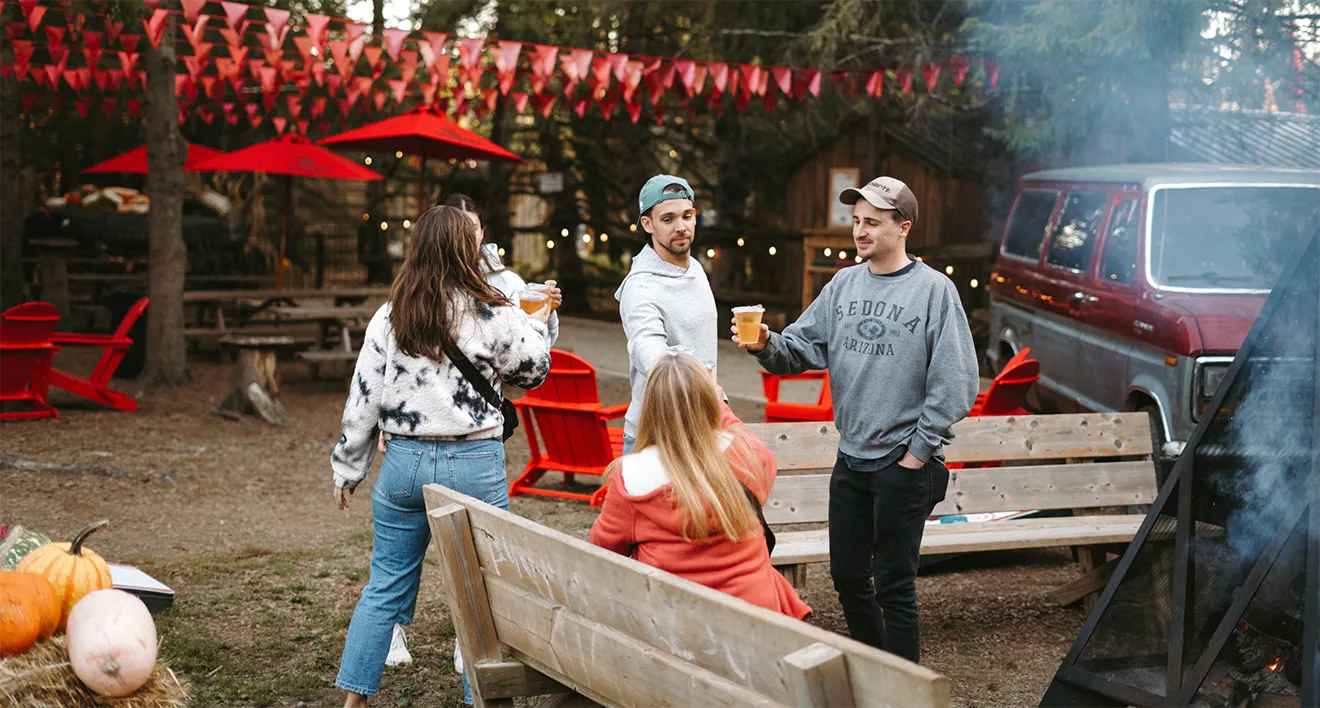 Friends gathering on outdoor patio at Macintosh's Ciderhouse with craft cider drinks, red umbrellas, and fire pit.
