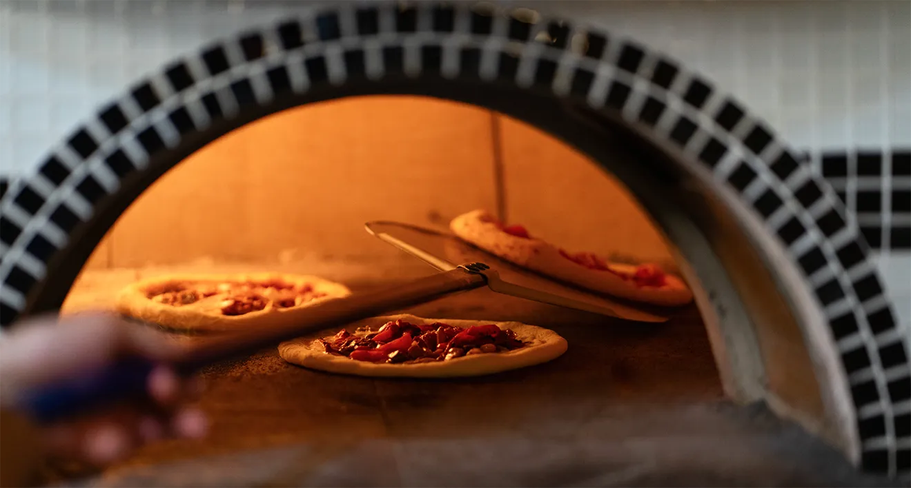 Fresh wood-fired pizzas baking inside custom tiled stone pizza oven at Saunders Farm.