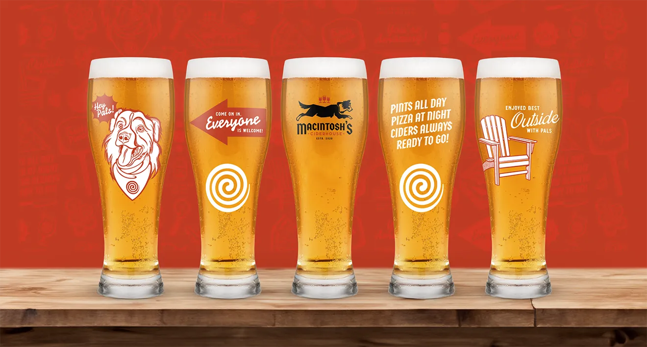 Macintosh's Ciderhouse custom branded glassware array filled with craft cider on wooden bar top by Hovski Studio.