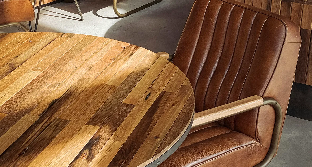 Round pieced raw wood dining table paired with leather armchair by Donahue Furniture.