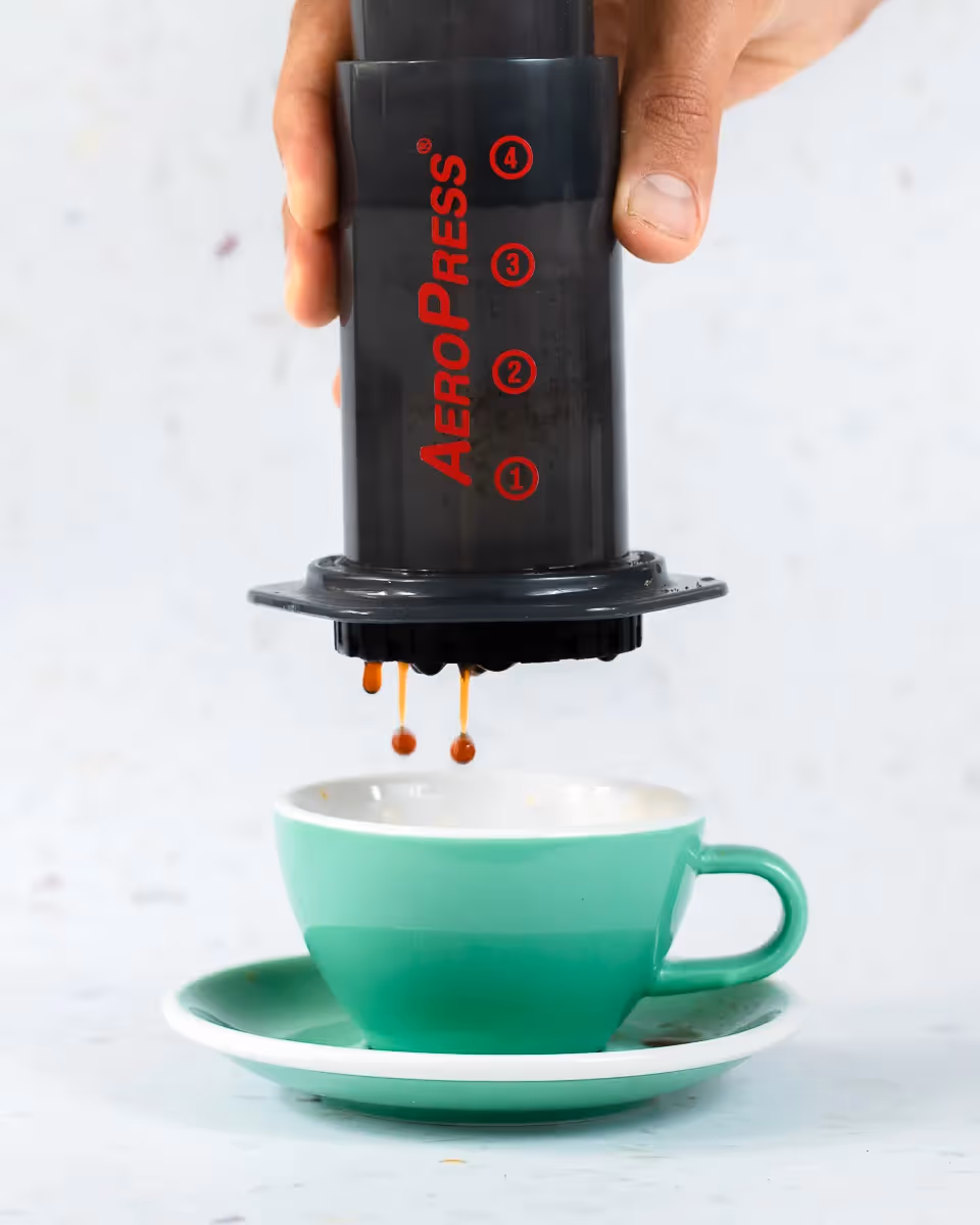 Man using AeroPress to little green coffee mug